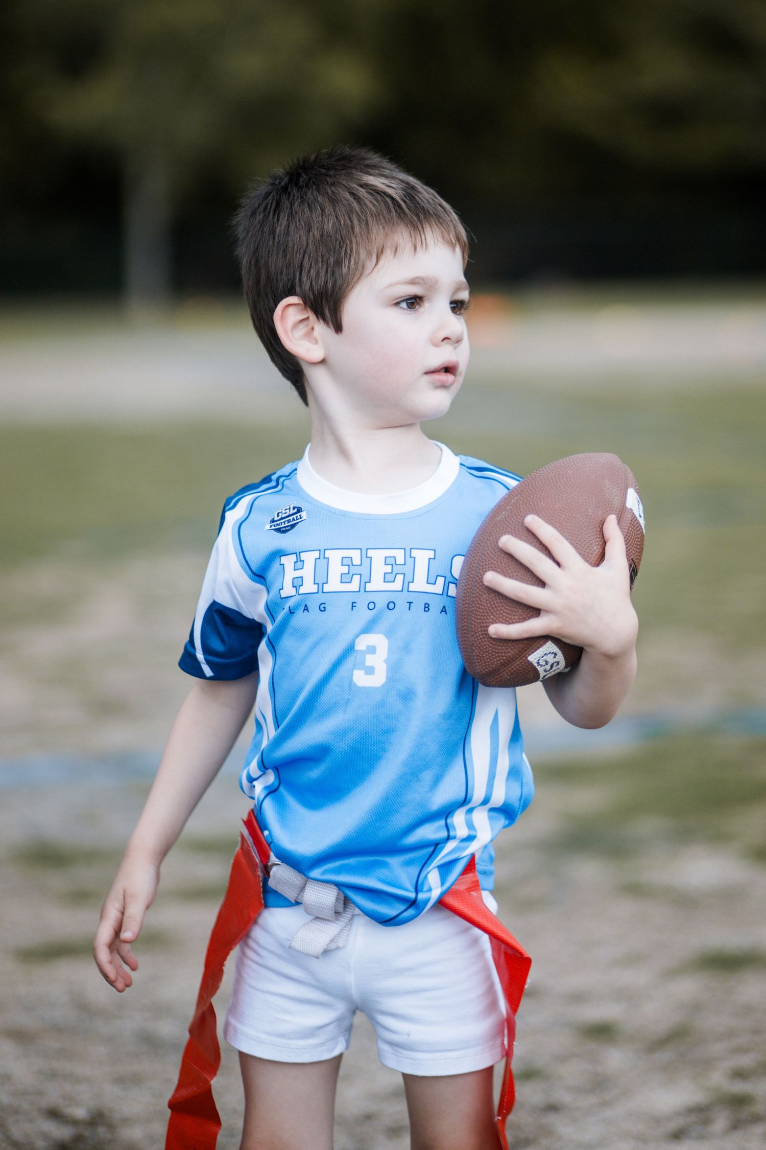 Young boy number 3 in light blue Heels jersey holding football on flag football field.