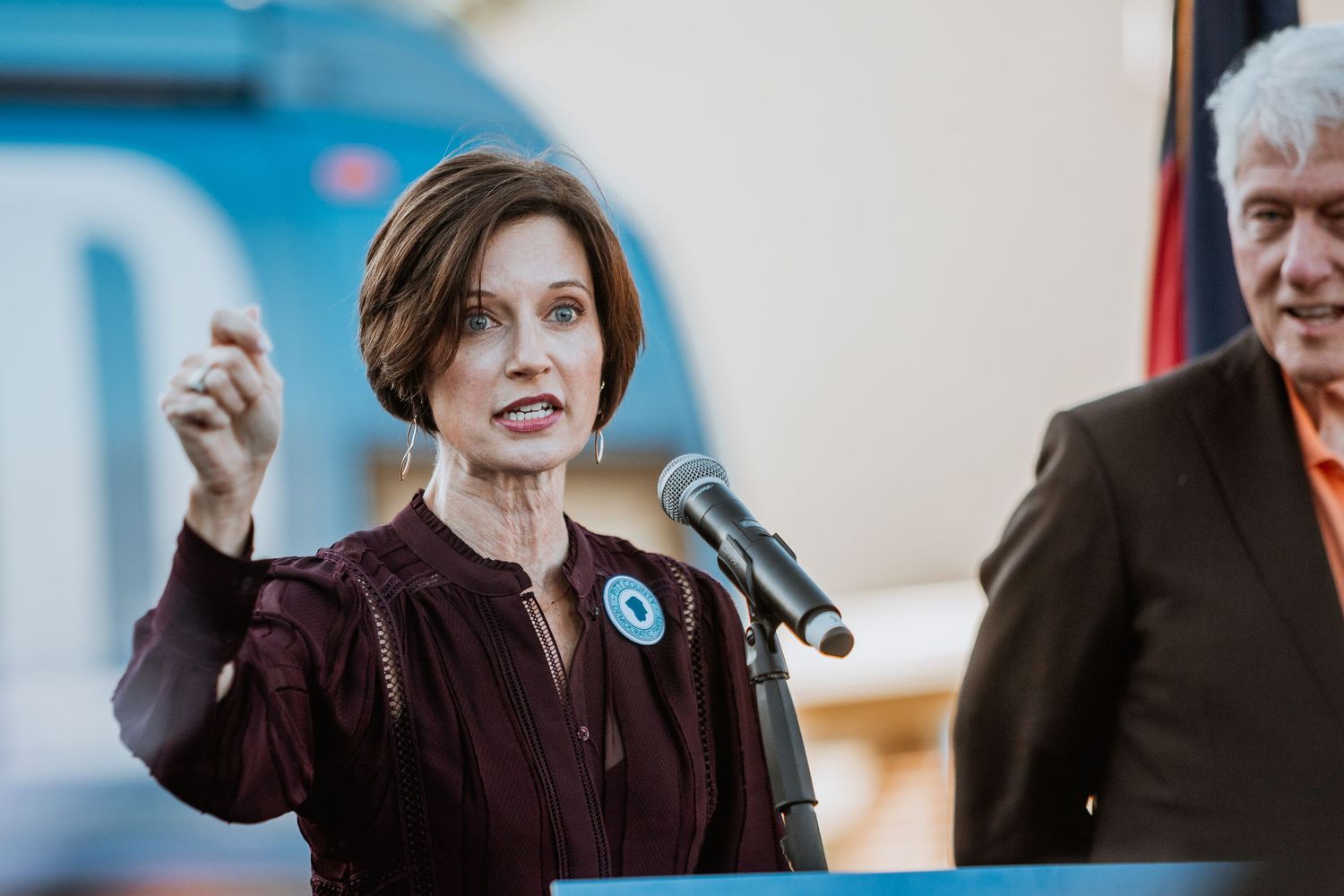 Woman in burgundy dress speaks passionately at podium during Harris Walz campaign rally event.