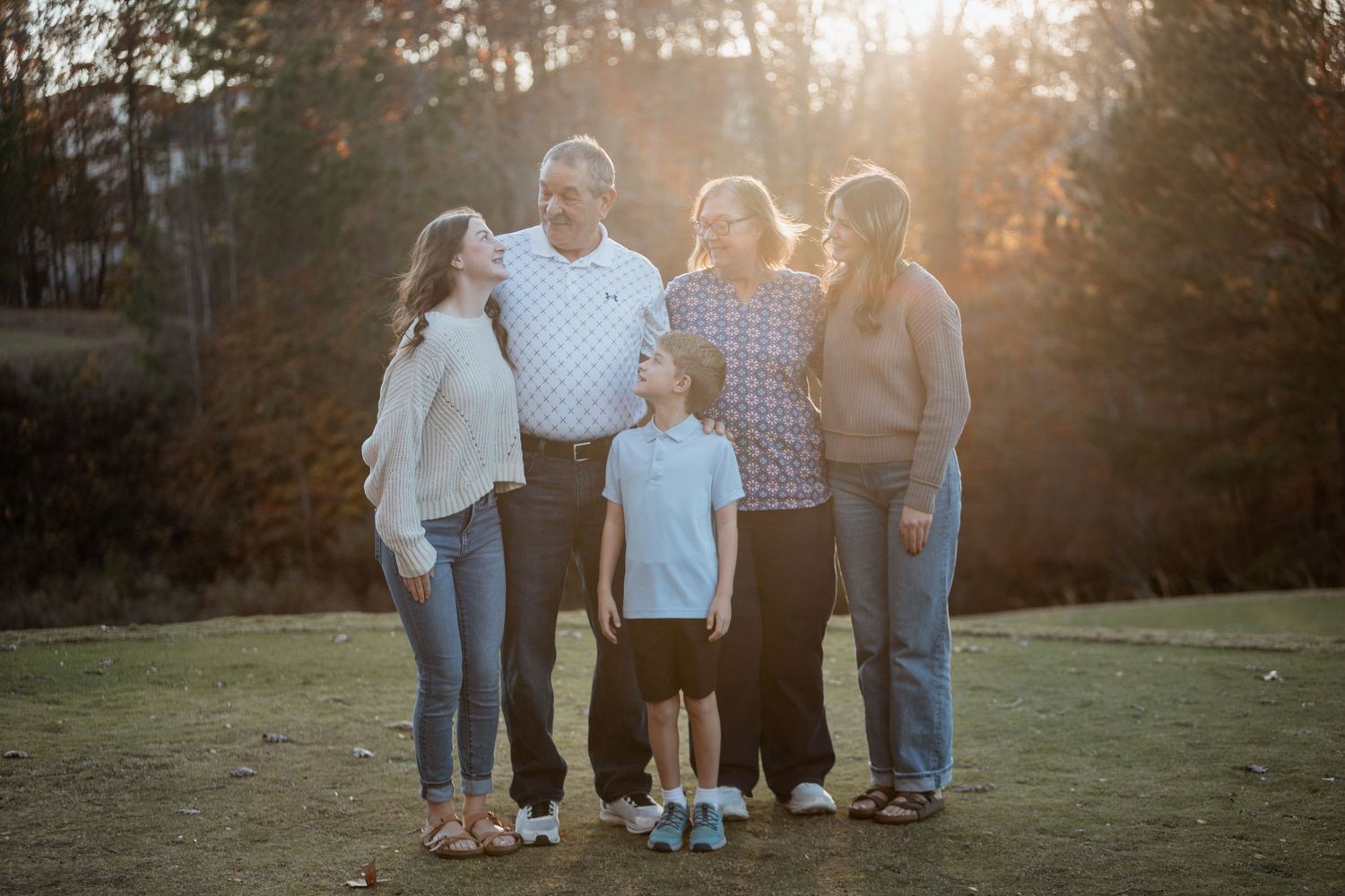 Family of five posing together outdoors in golden sunset light surrounded by trees.