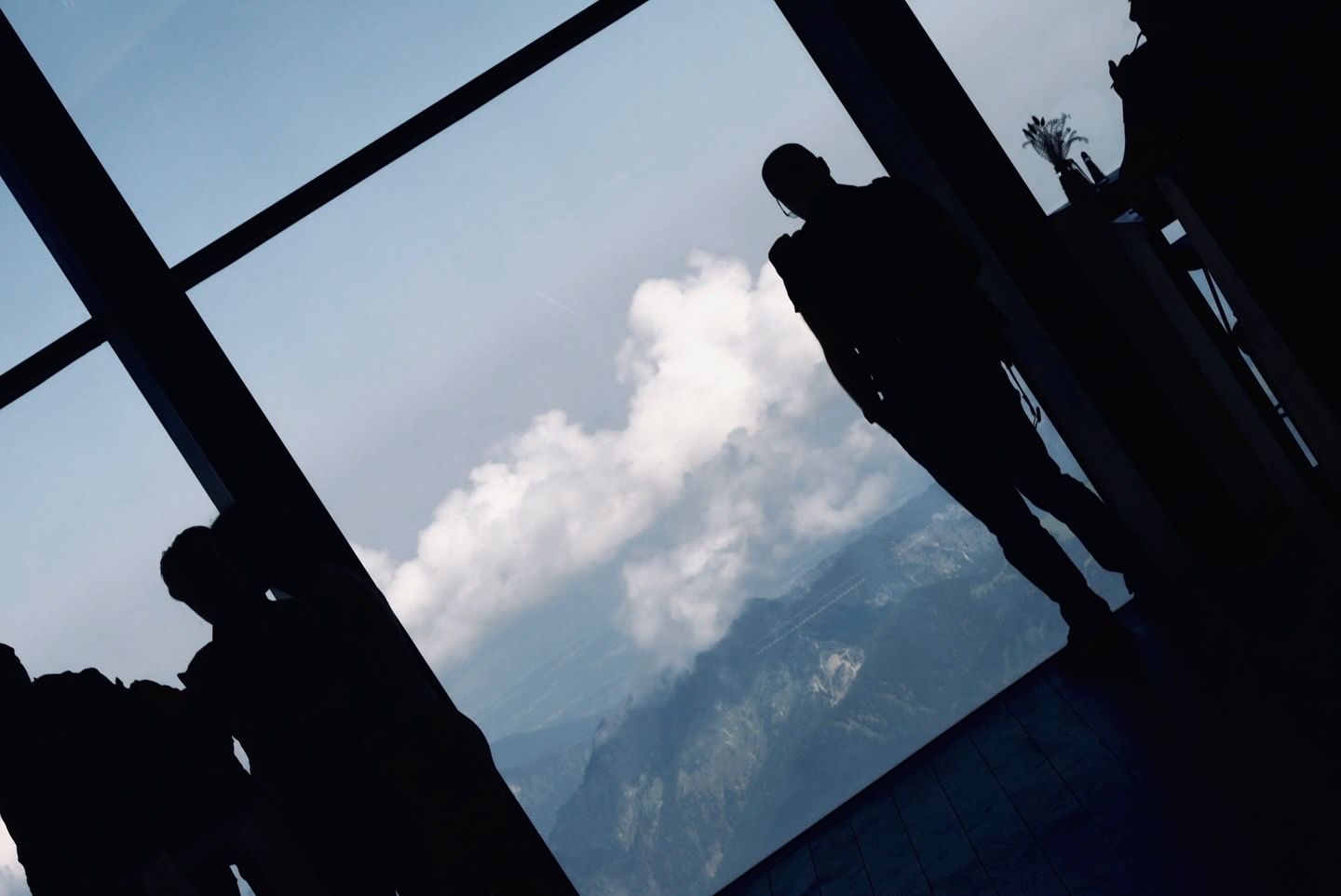 Silhouetted figures standing before large windows with dramatic mountain and cloud views.