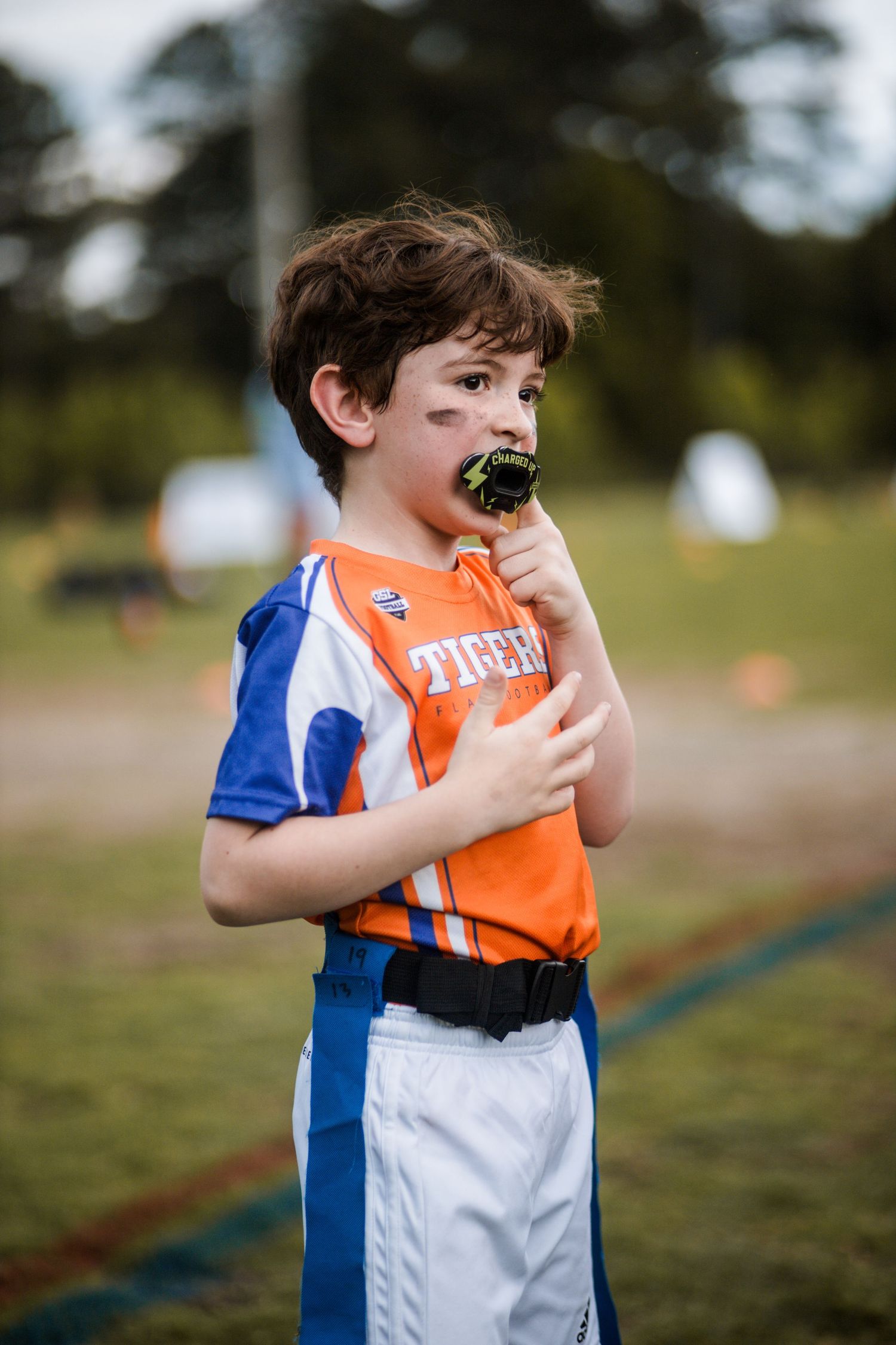 Young boy in orange Tigers jersey wearing black mouthguard during youth flag football.