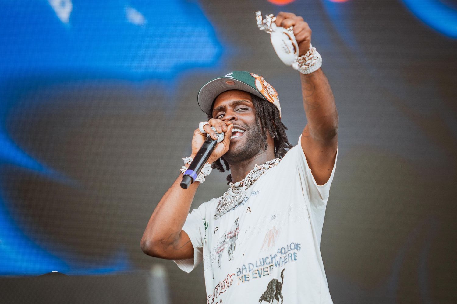 Energetic performer singing into a microphone on stage wearing a graphic tee and cap at a live concert.