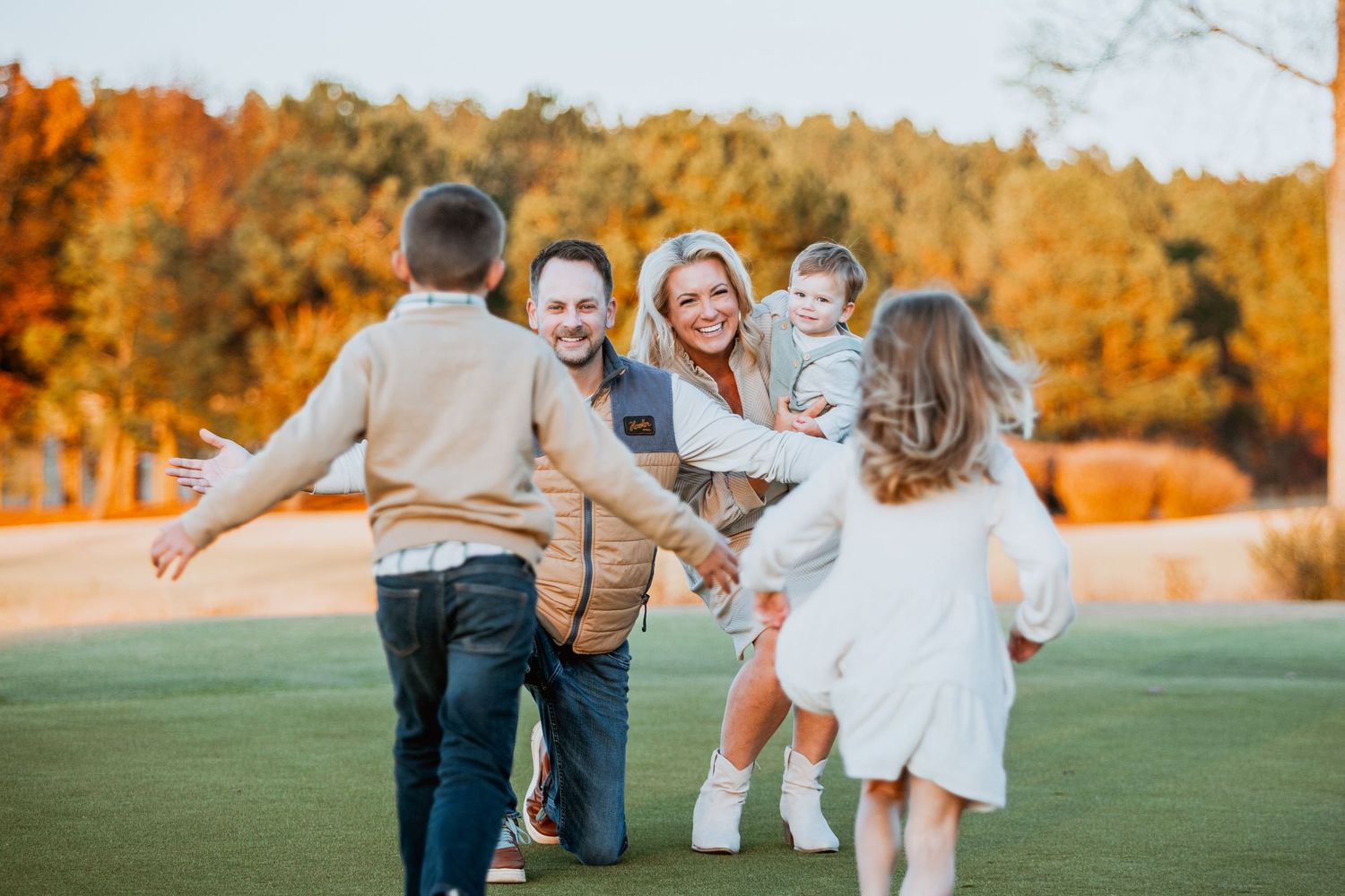 Family reuniting with open arms on a golf course surrounded by autumn trees.