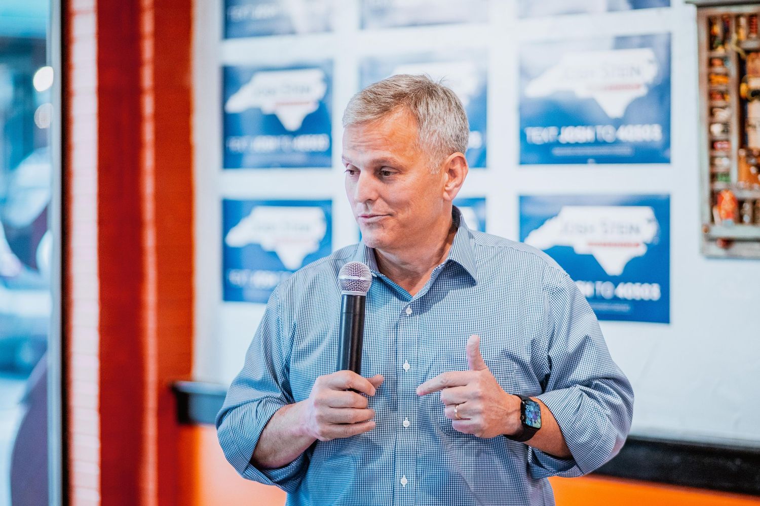 Man in blue shirt giving thumbs up while speaking at political campaign event.