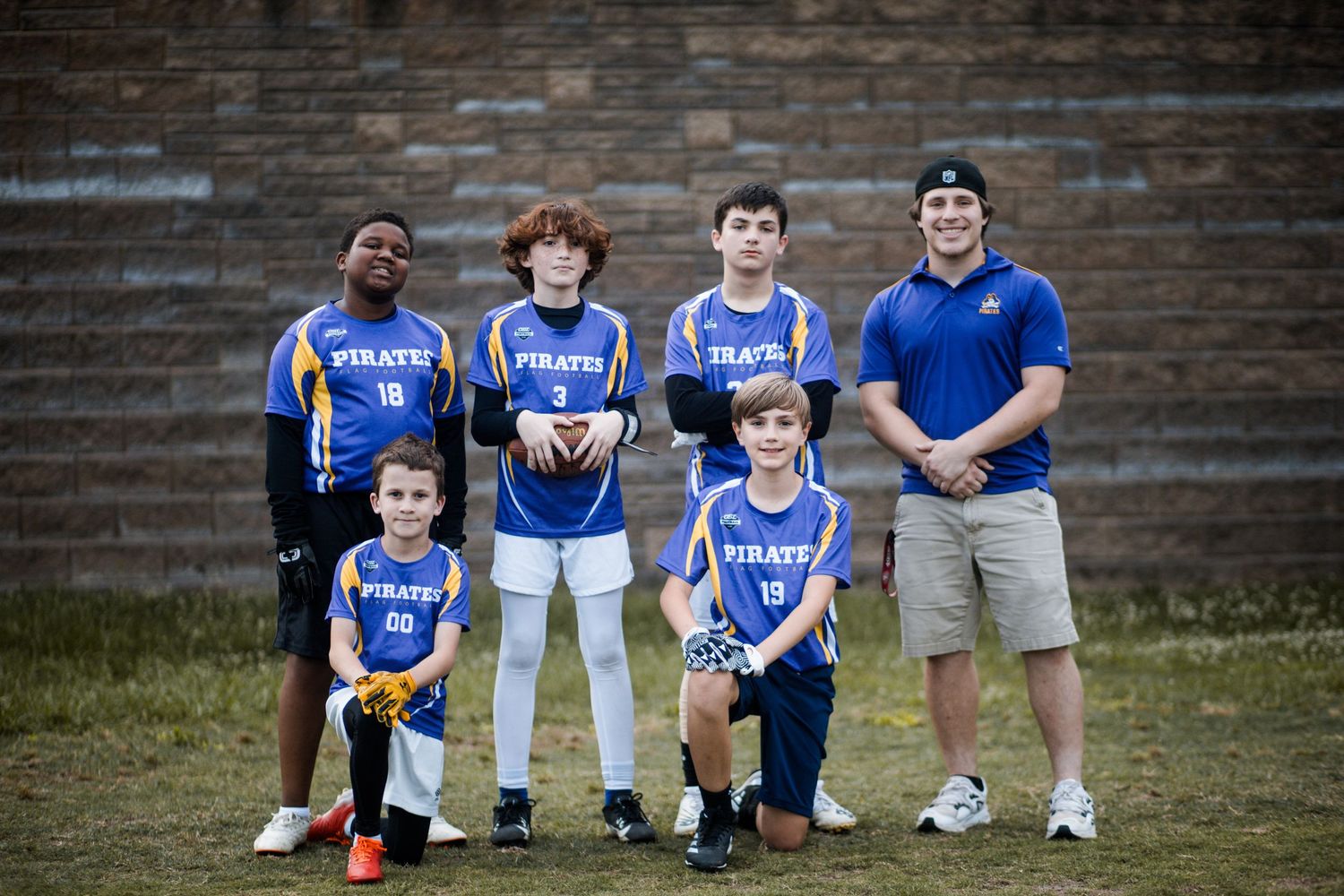 Small youth flag football team in blue Pirates uniforms posing with coach outdoors.