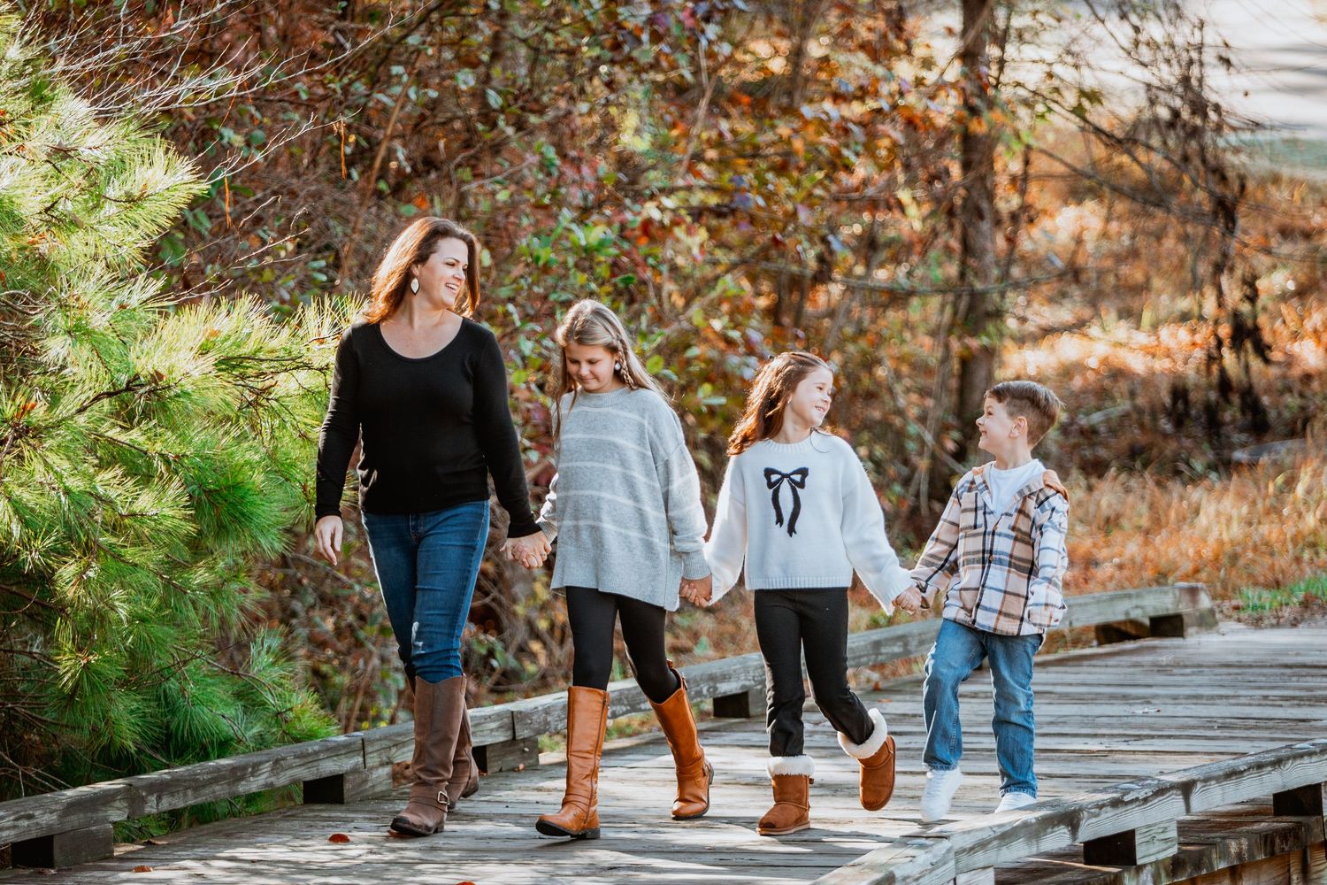 Mother walking with three children holding hands on wooden bridge during fall family portrait.