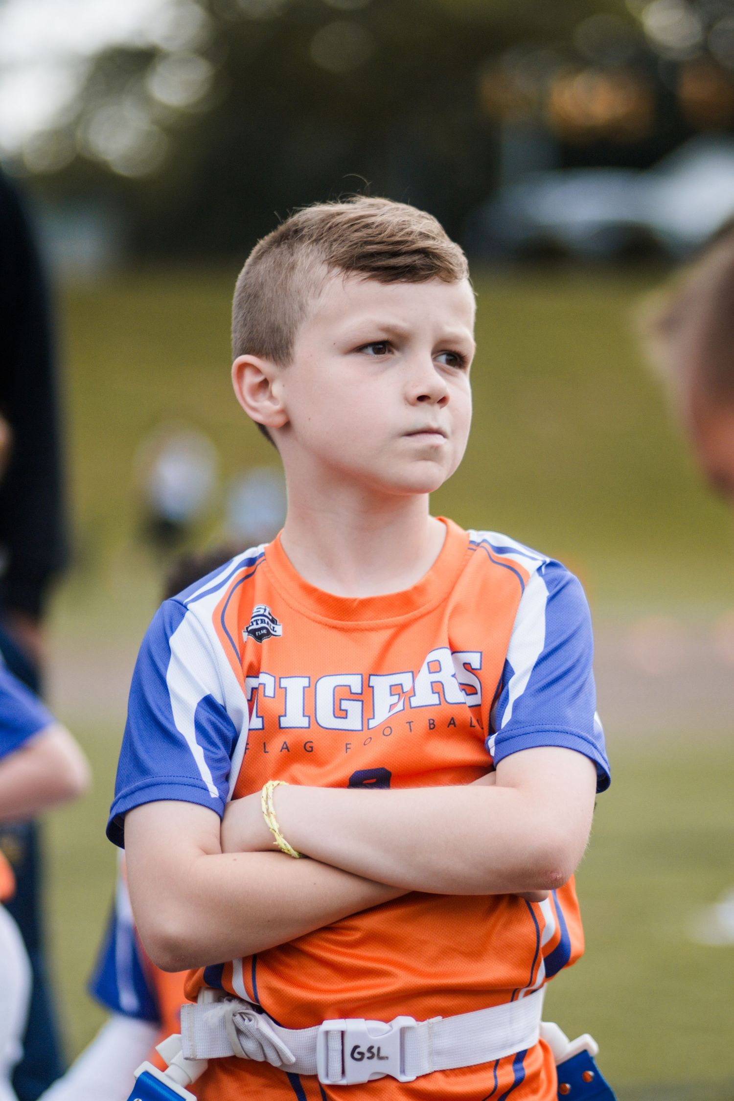 Young boy in Tigers orange flag football jersey standing with arms crossed.
