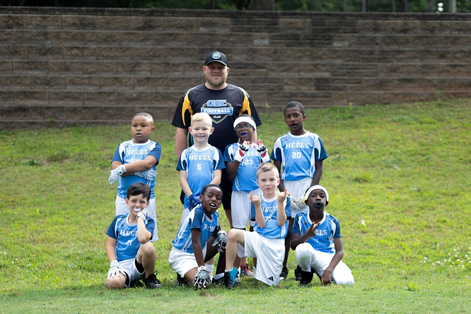 Young soccer team in blue and white uniforms poses with coach on a green grass field.