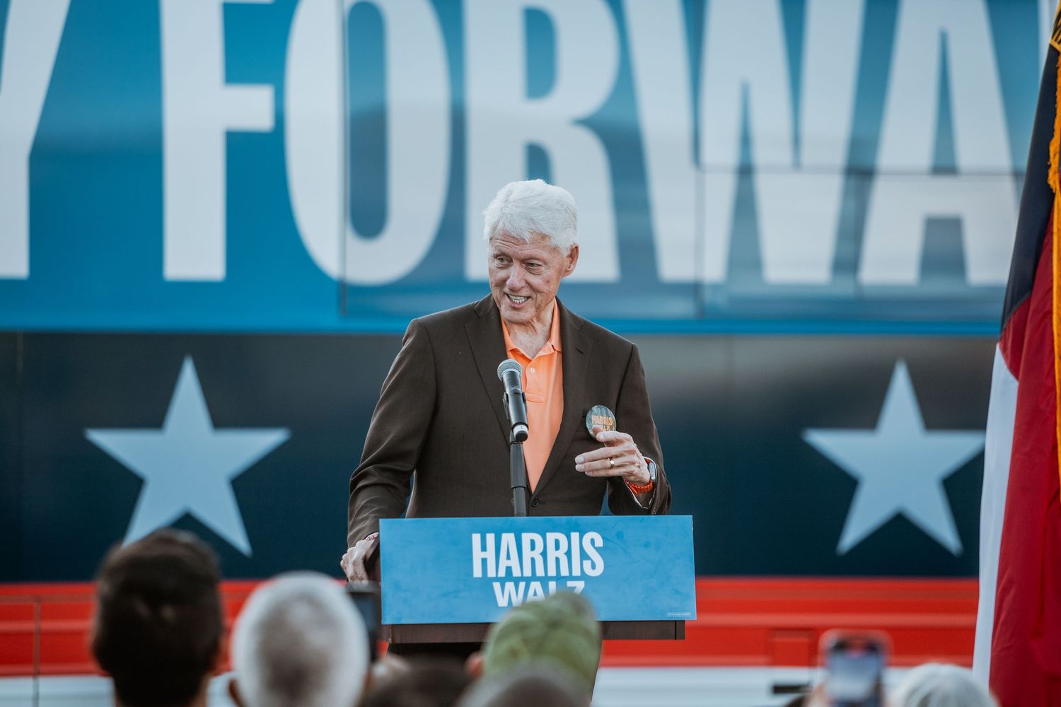 Man speaking at a Harris Walz campaign rally in front of a blue banner with stars.