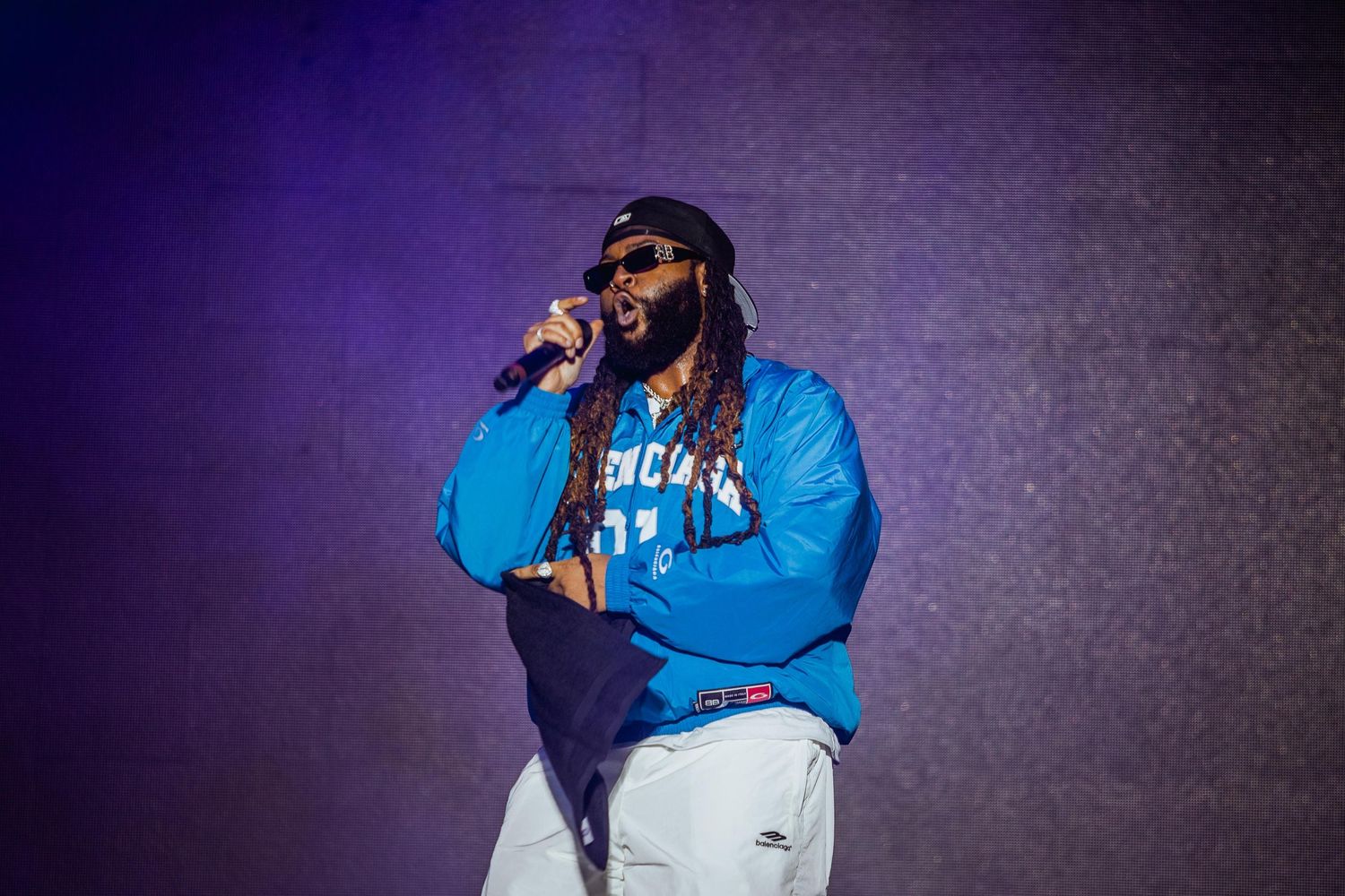 Male rapper in blue hoodie performing on stage with microphone.
