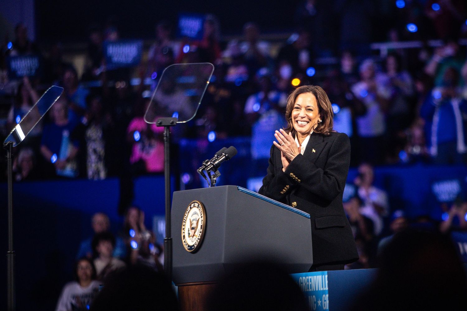 Kamala Harris applauds at podium during 2024 presidential campaign rally.