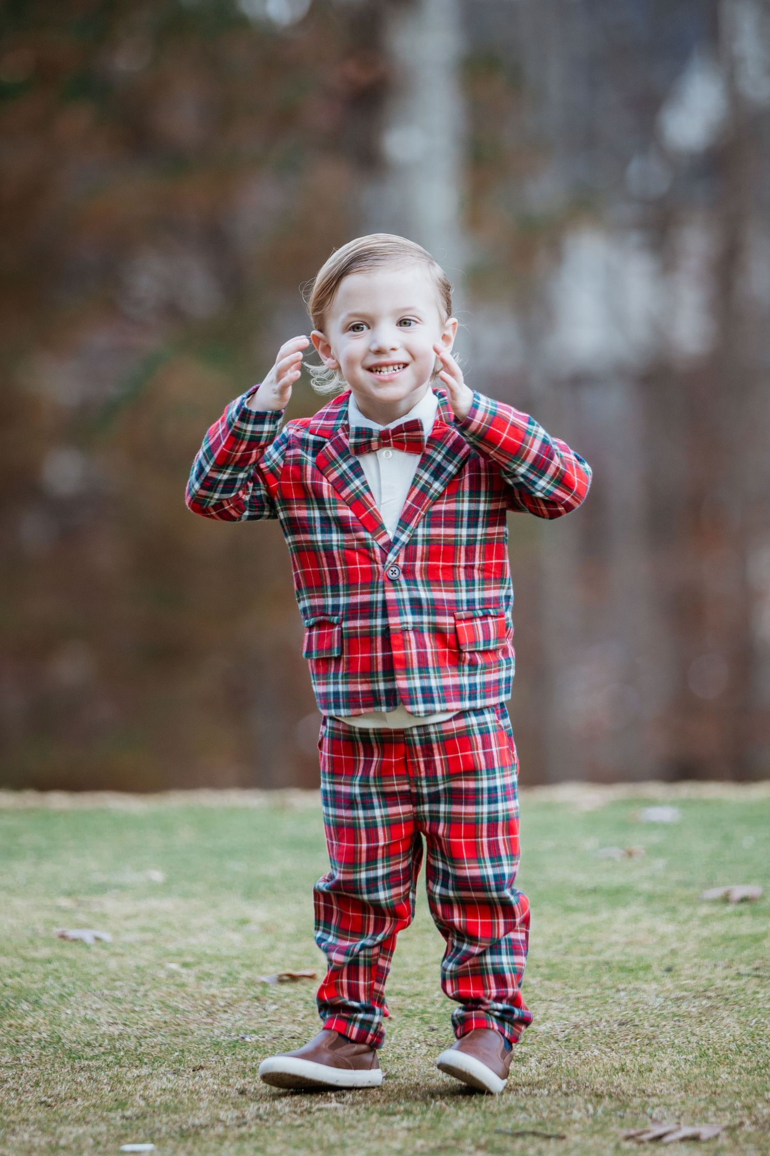 Happy young boy in red tartan plaid suit and bow tie posing outdoors.