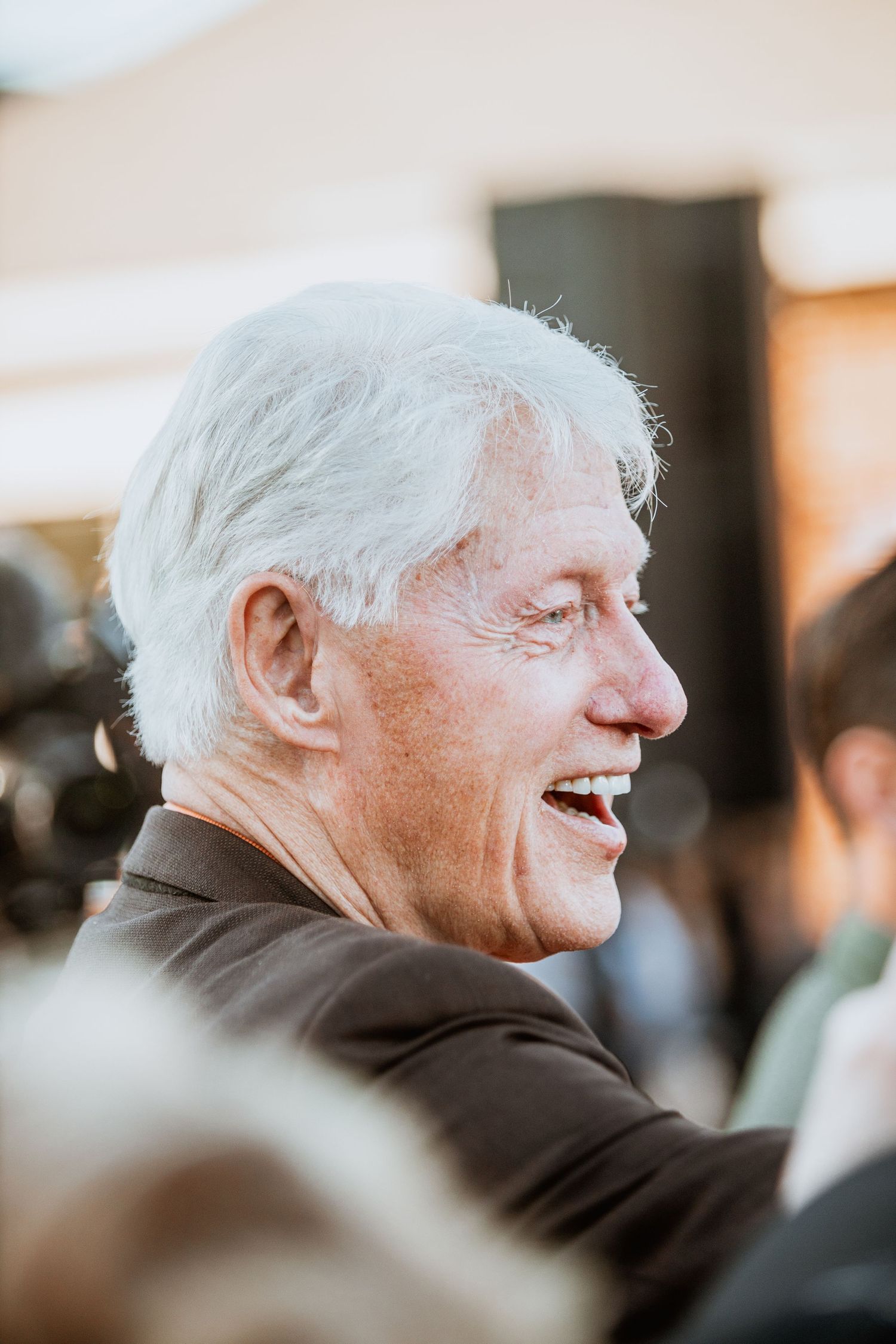 Elderly man with white hair laughing joyfully in profile view at an outdoor event.
