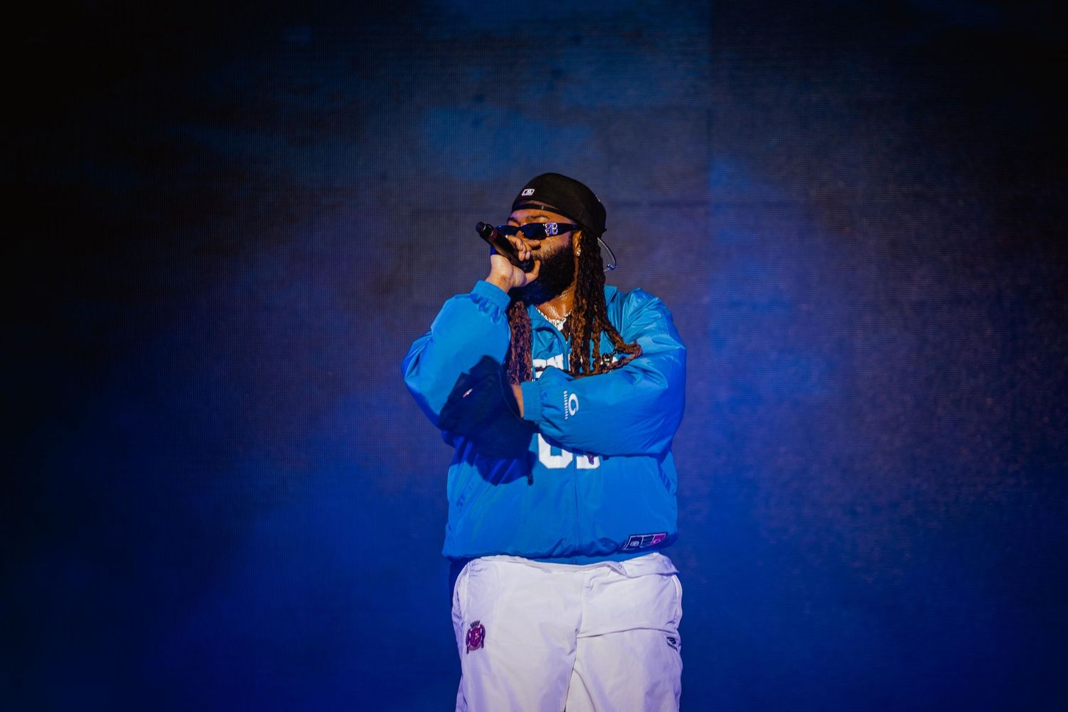 Male rapper in blue hoodie performing on blue-lit stage.