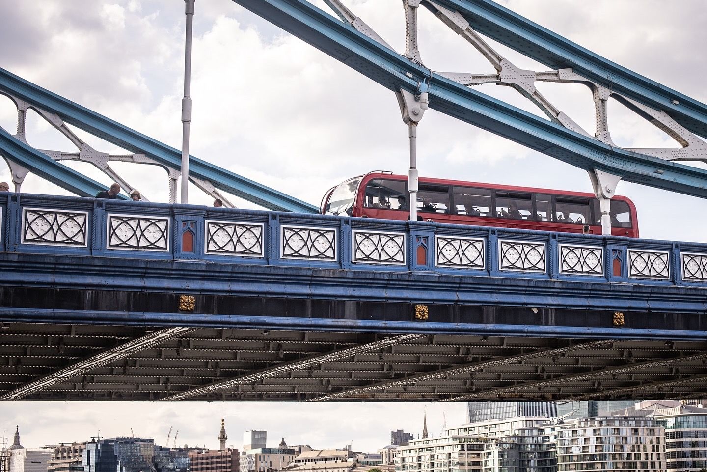 A red double-decker bus crossing the ornate Tower Bridge in London, England.
