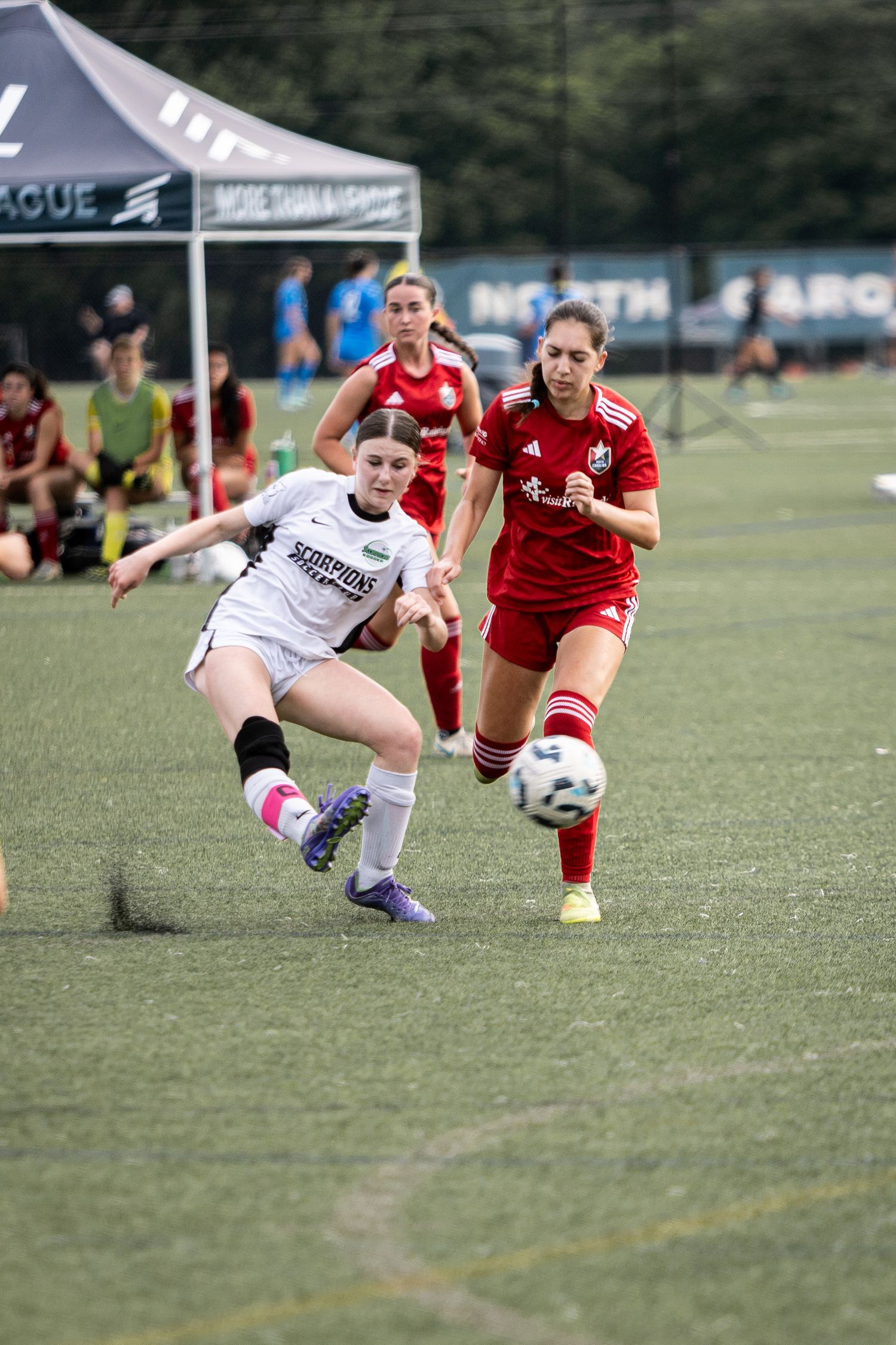 Scorpions female soccer player strikes ball while red-uniformed opponent closes in during competitive match.