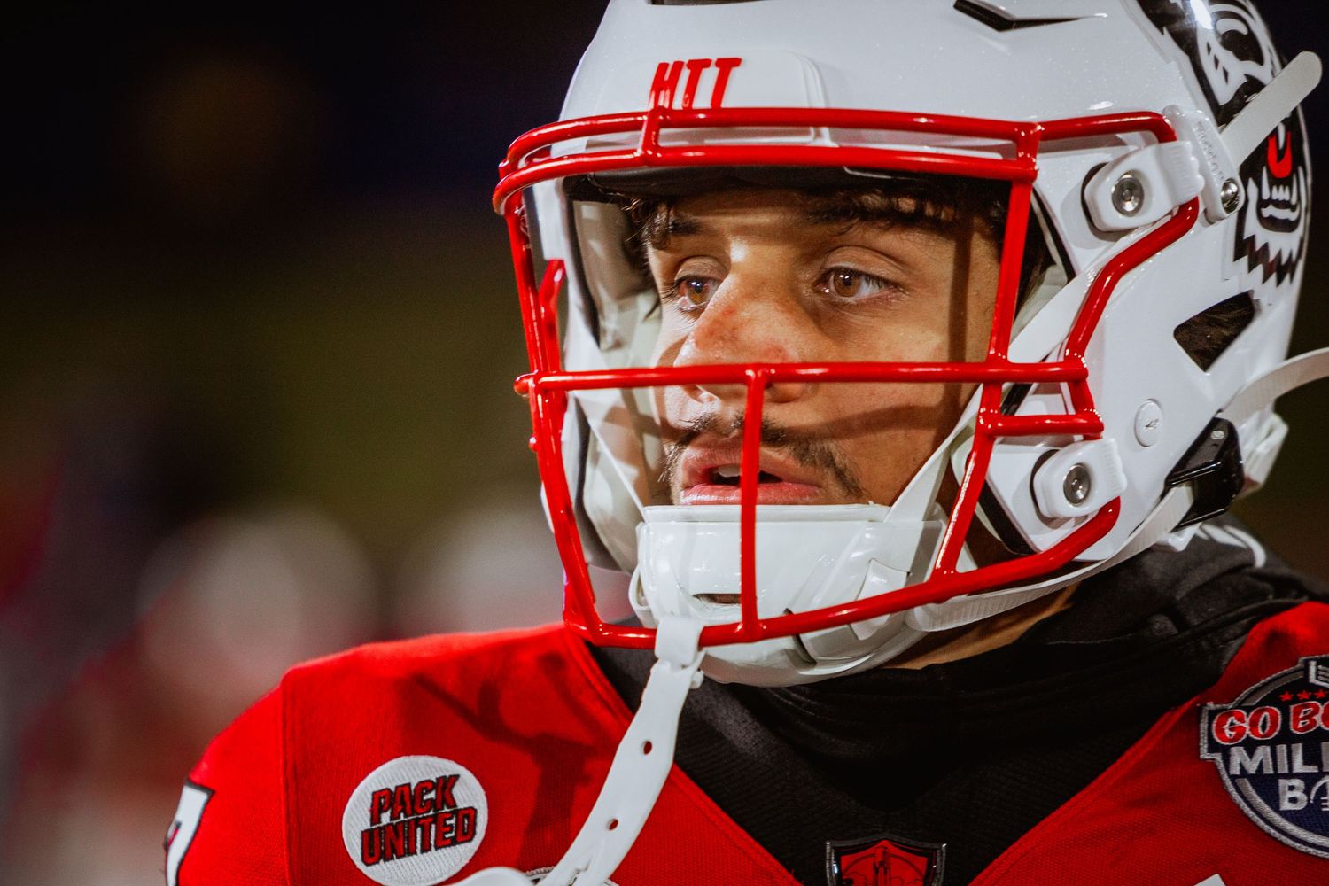 NC State Wolfpack football player in red helmet and uniform with face visible through visor during night game.
