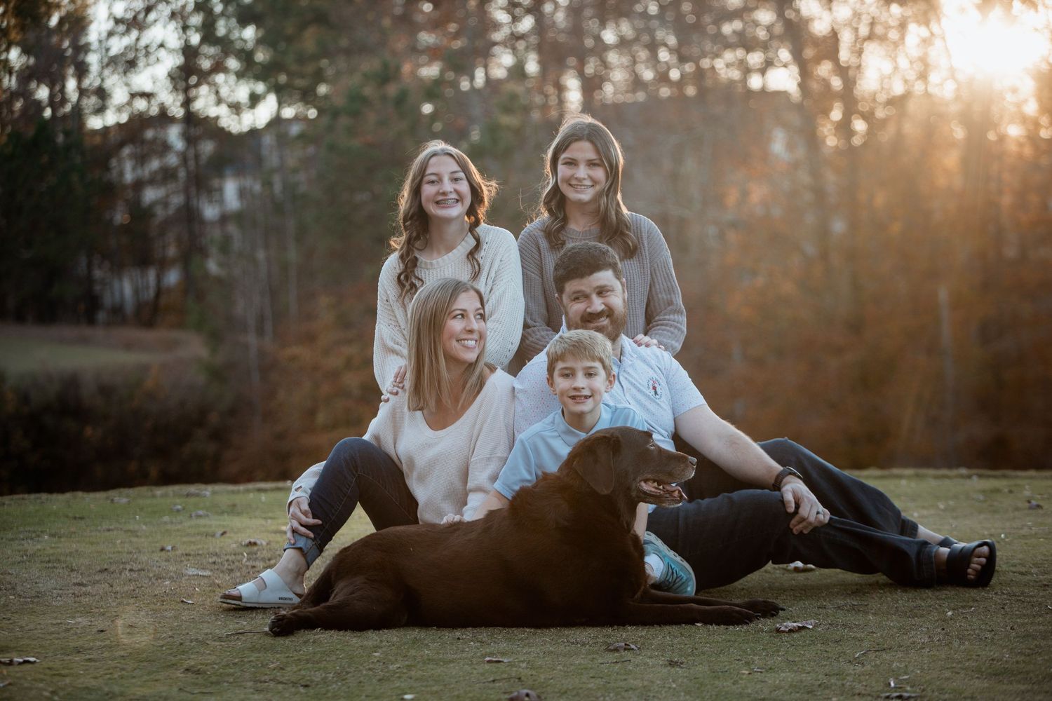 Cheerful family of five laughing together with their chocolate Labrador in a fall outdoor portrait.