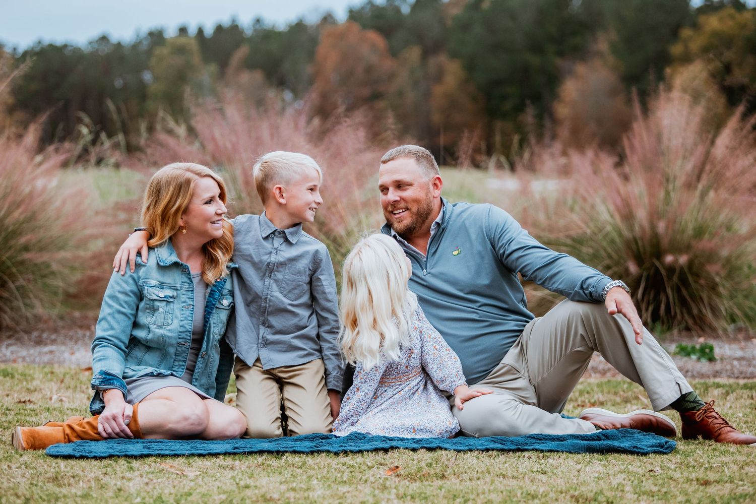 Happy family of four sitting on a blanket in a scenic autumn outdoor setting.