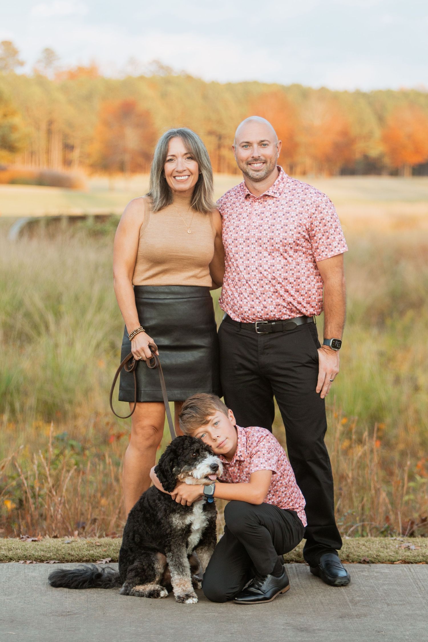 Family portrait with bernedoodle dog in autumn setting, son crouching beside pet outdoors.