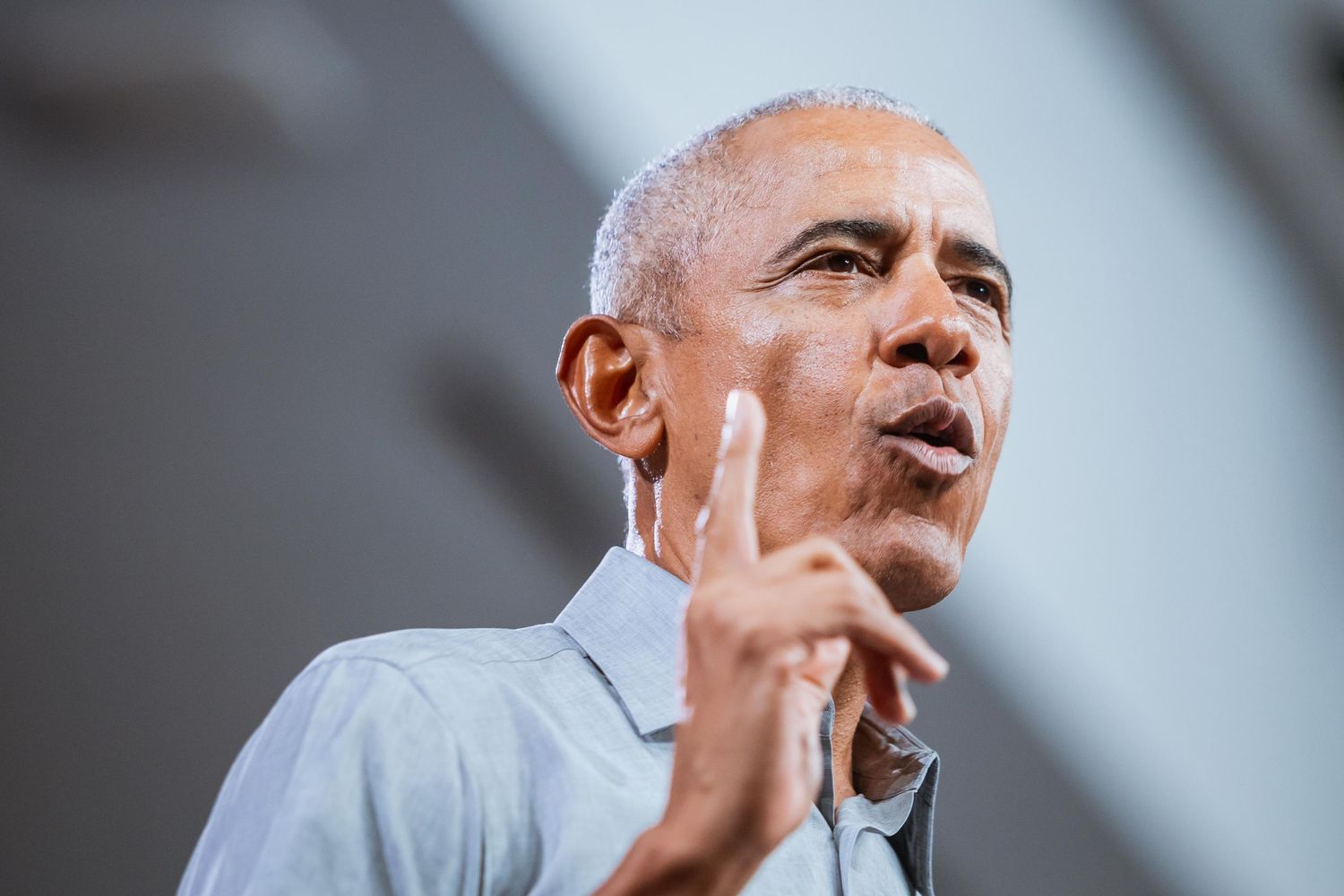 A man gestures with two fingers while delivering a speech at an indoor event.