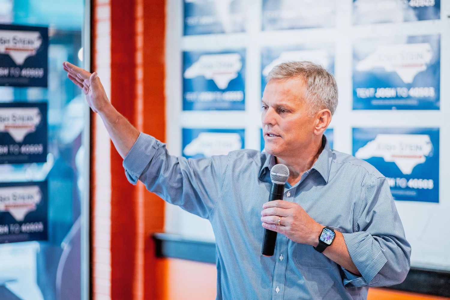 Man gesturing with raised hand while holding microphone at campaign event.
