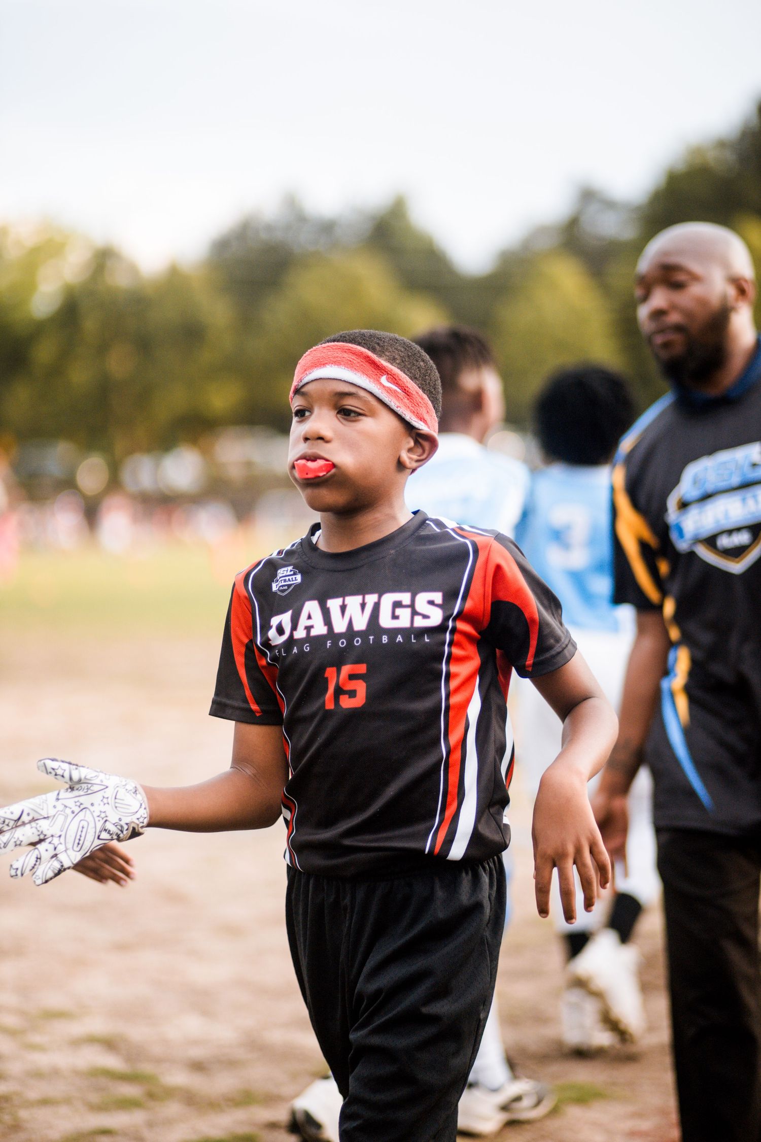 Young boy in Dawgs #15 flag football uniform with mouthguard at outdoor event.