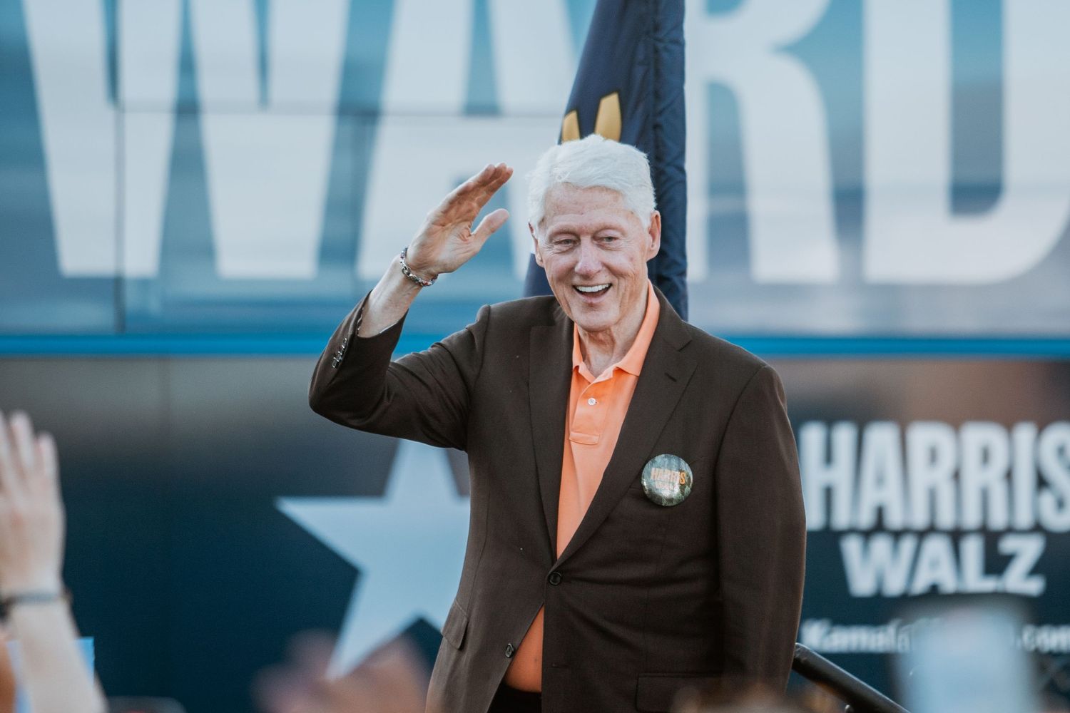 White-haired man waves to crowd at Harris Walz 2024 campaign rally.