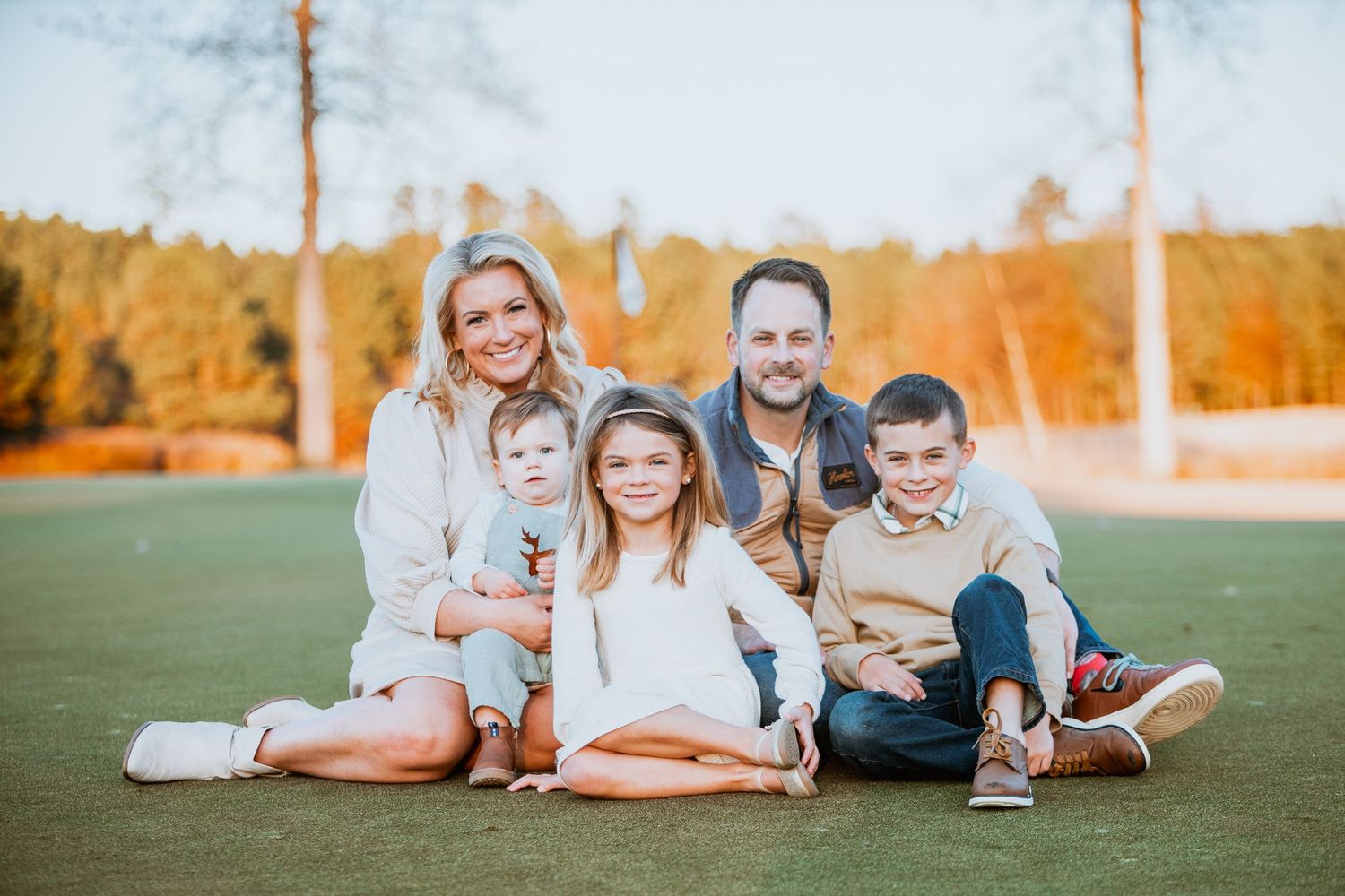 Smiling family of five posing together on a golf course at golden hour.