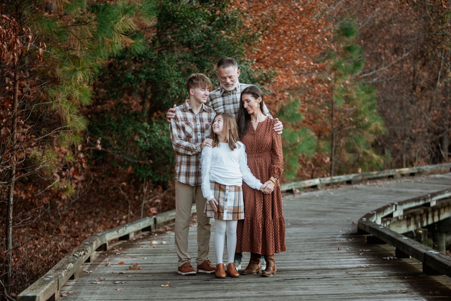 Family of four posing together on a wooden boardwalk surrounded by autumn foliage.