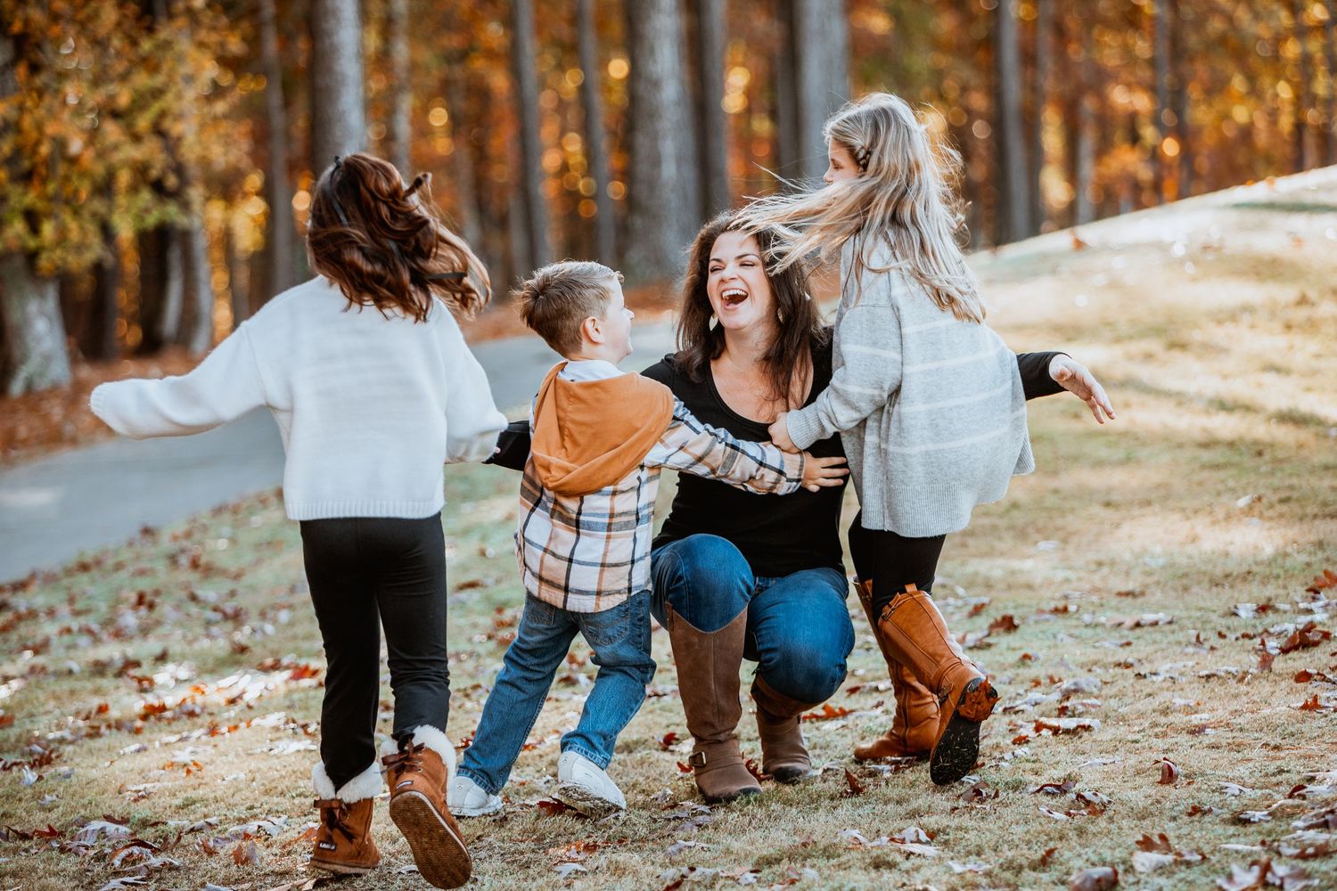 Laughing mother playing joyfully with her three children in a vibrant fall outdoor landscape.