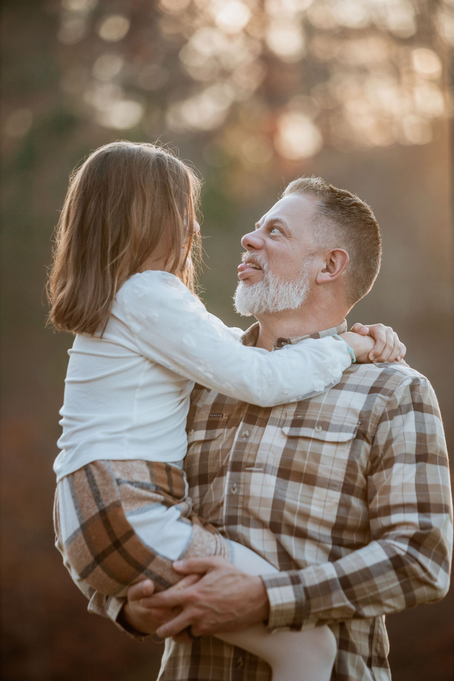 Bearded father gazing lovingly at daughter he holds in arms outdoors in golden light.