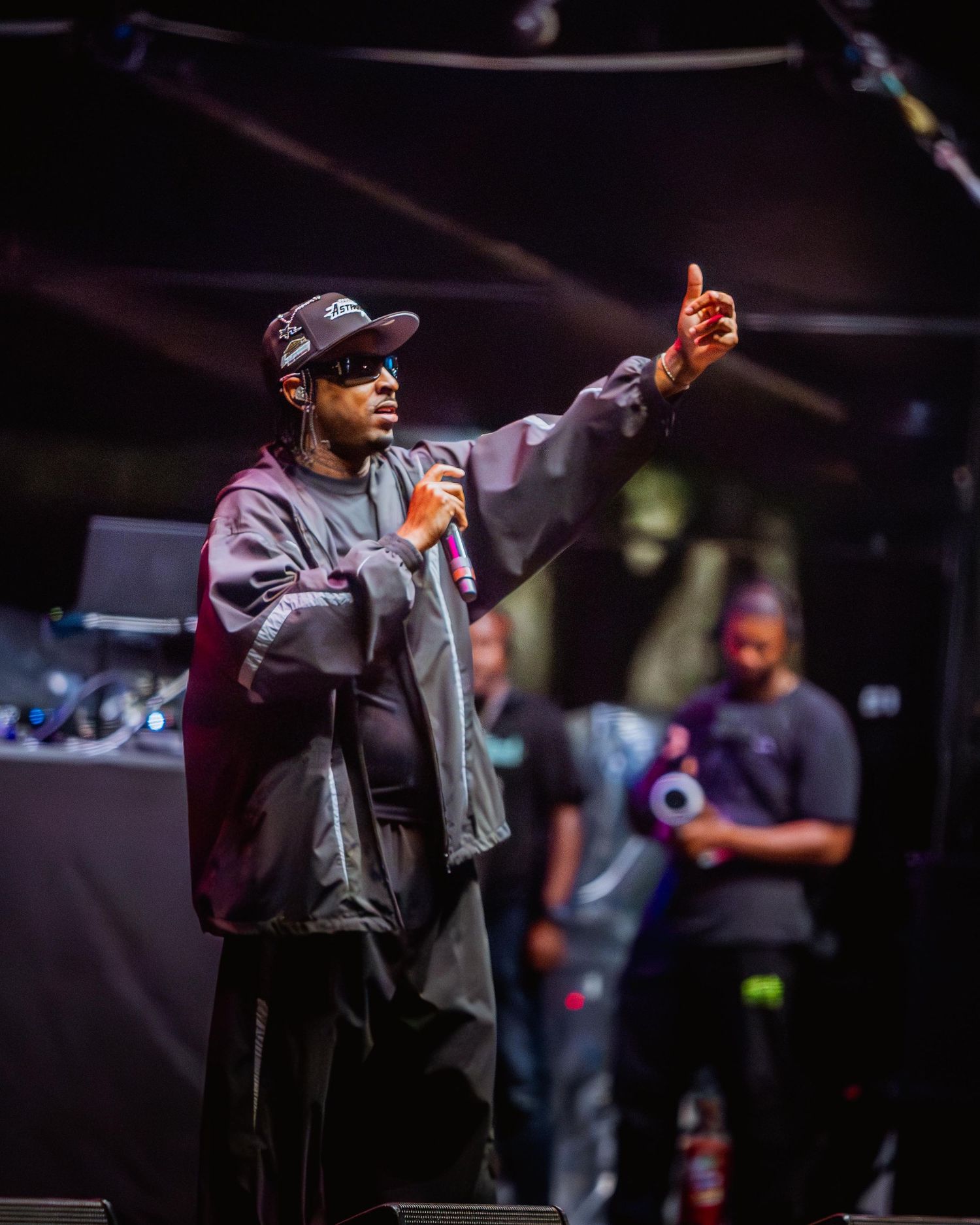 Male rapper in dark jacket gesturing on outdoor festival stage.