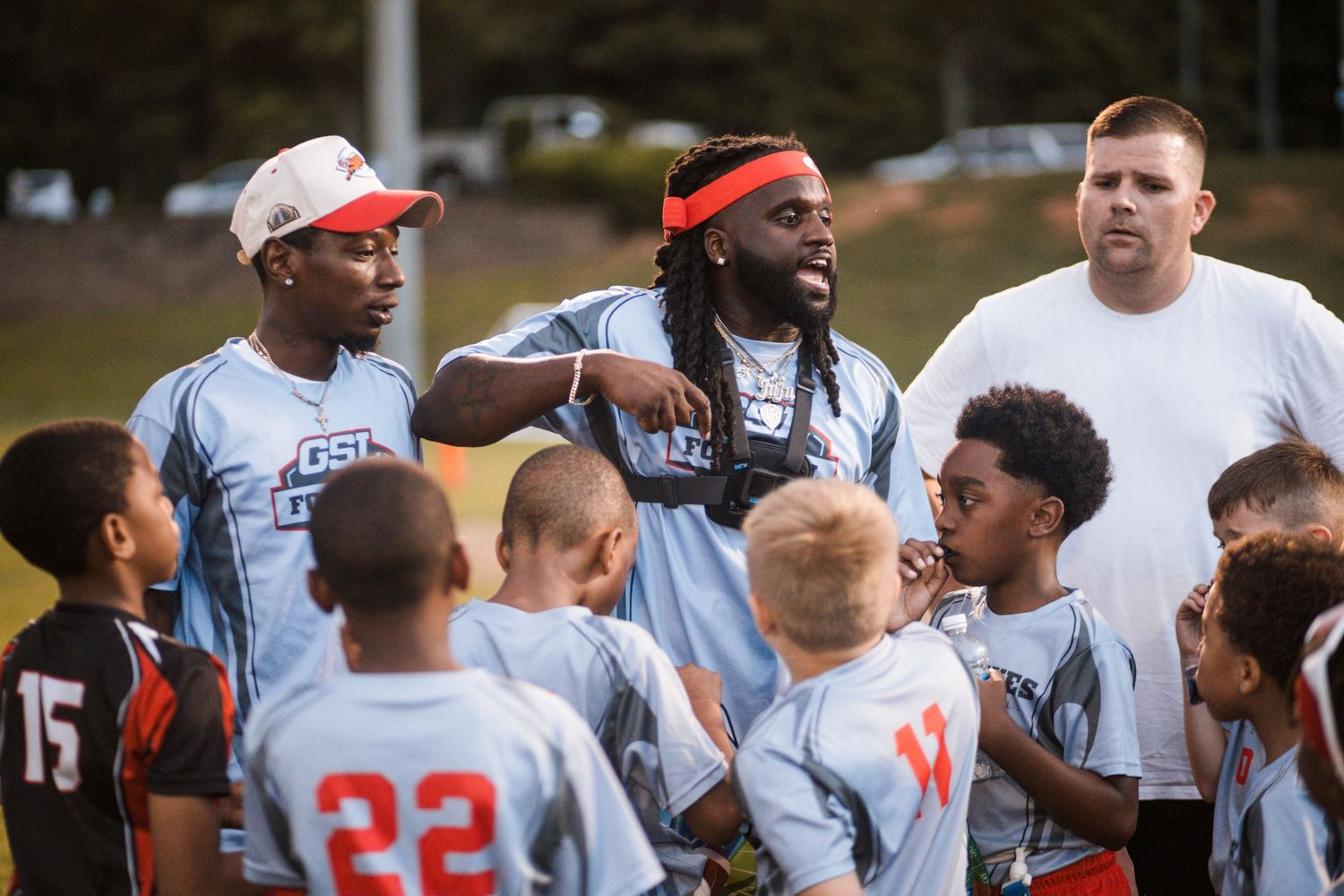 Adult coaches talk to a group of young flag football players during an outdoor youth game.