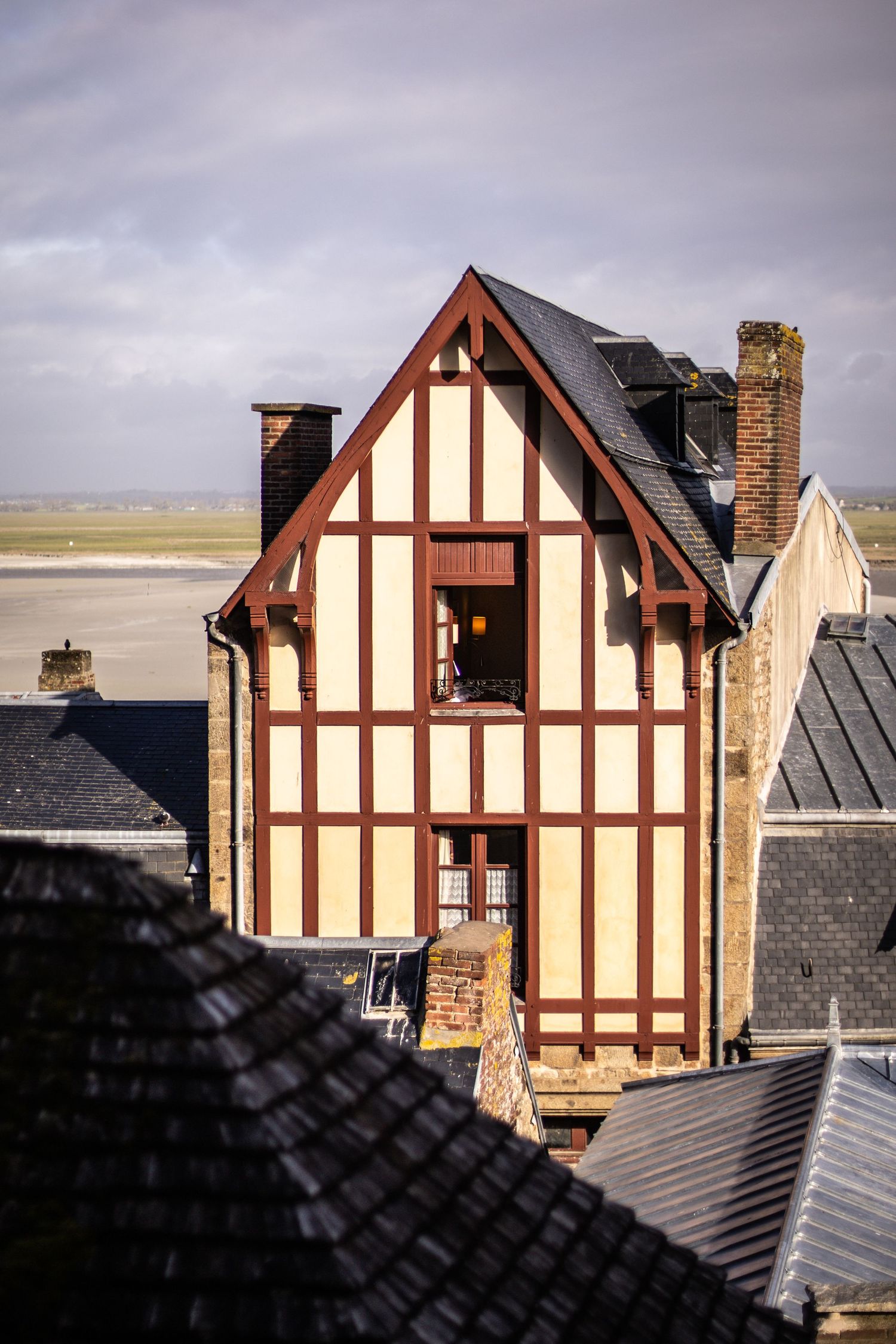 Traditional half-timbered house with red wooden beams at Mont Saint-Michel with coastal flats behind.