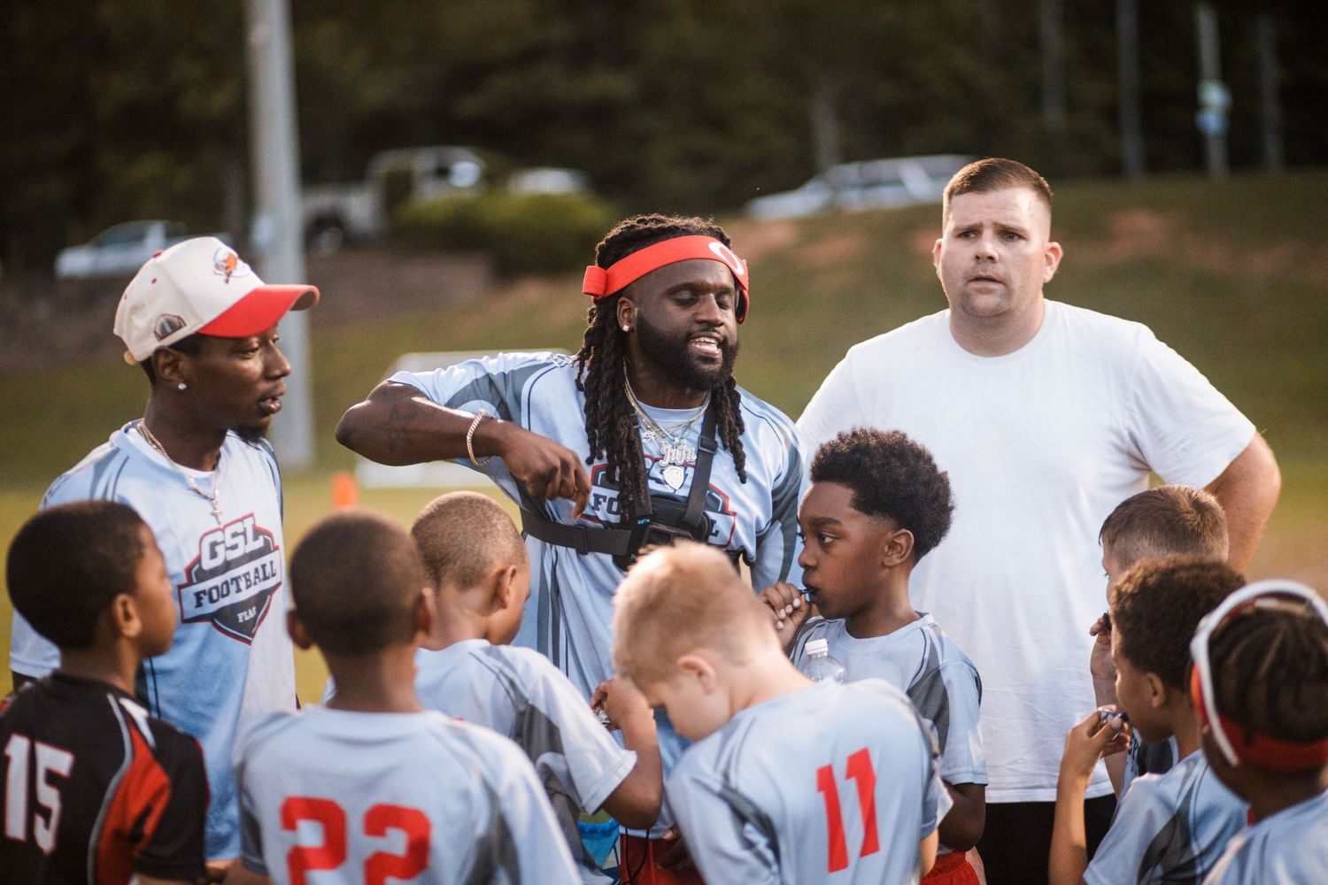 Coaches in blue jerseys give instructions to young flag football players during an outdoor game.