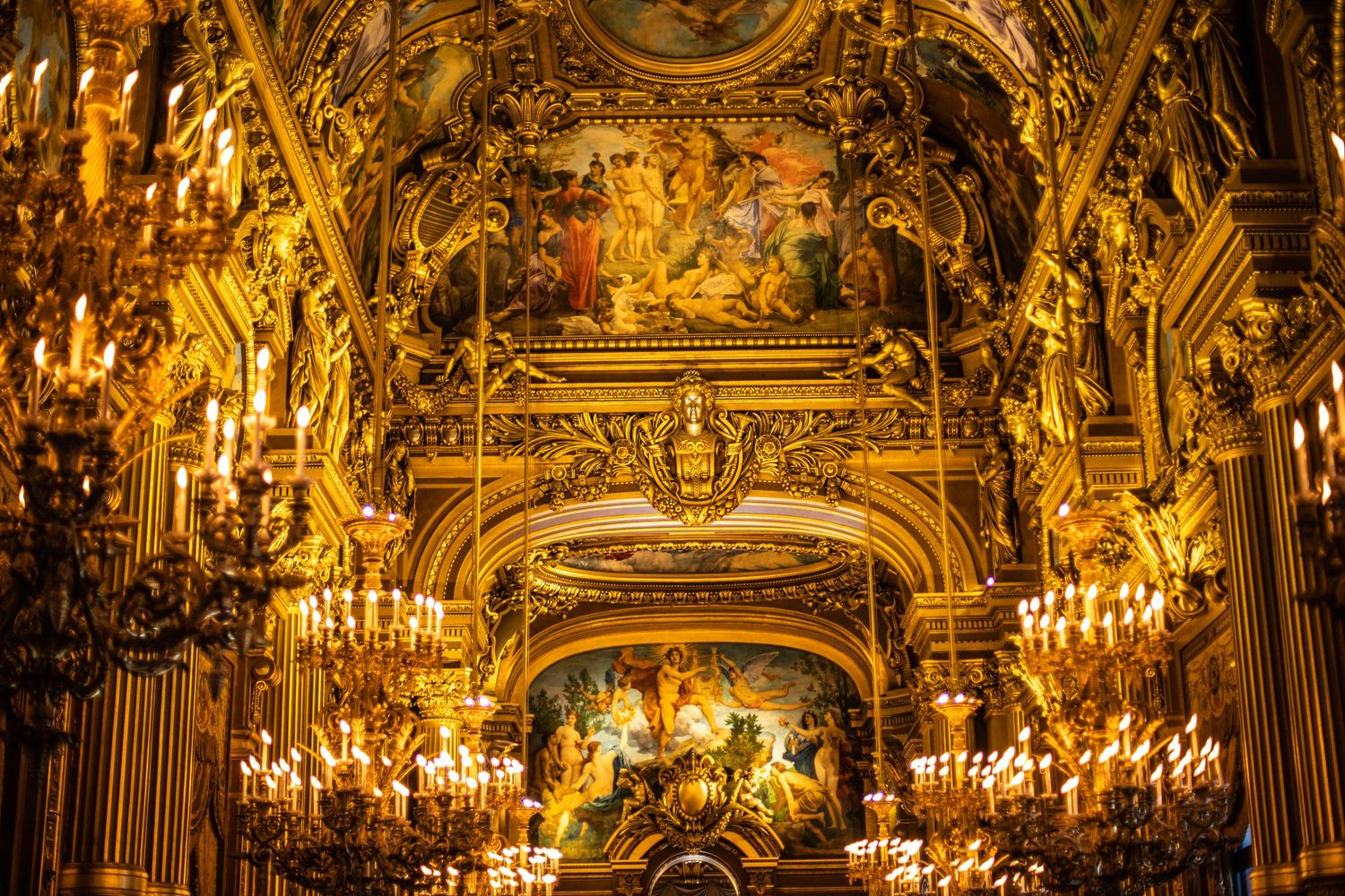 Ornate golden interior of the Paris Opera Garnier with chandeliers and elaborate ceiling murals.