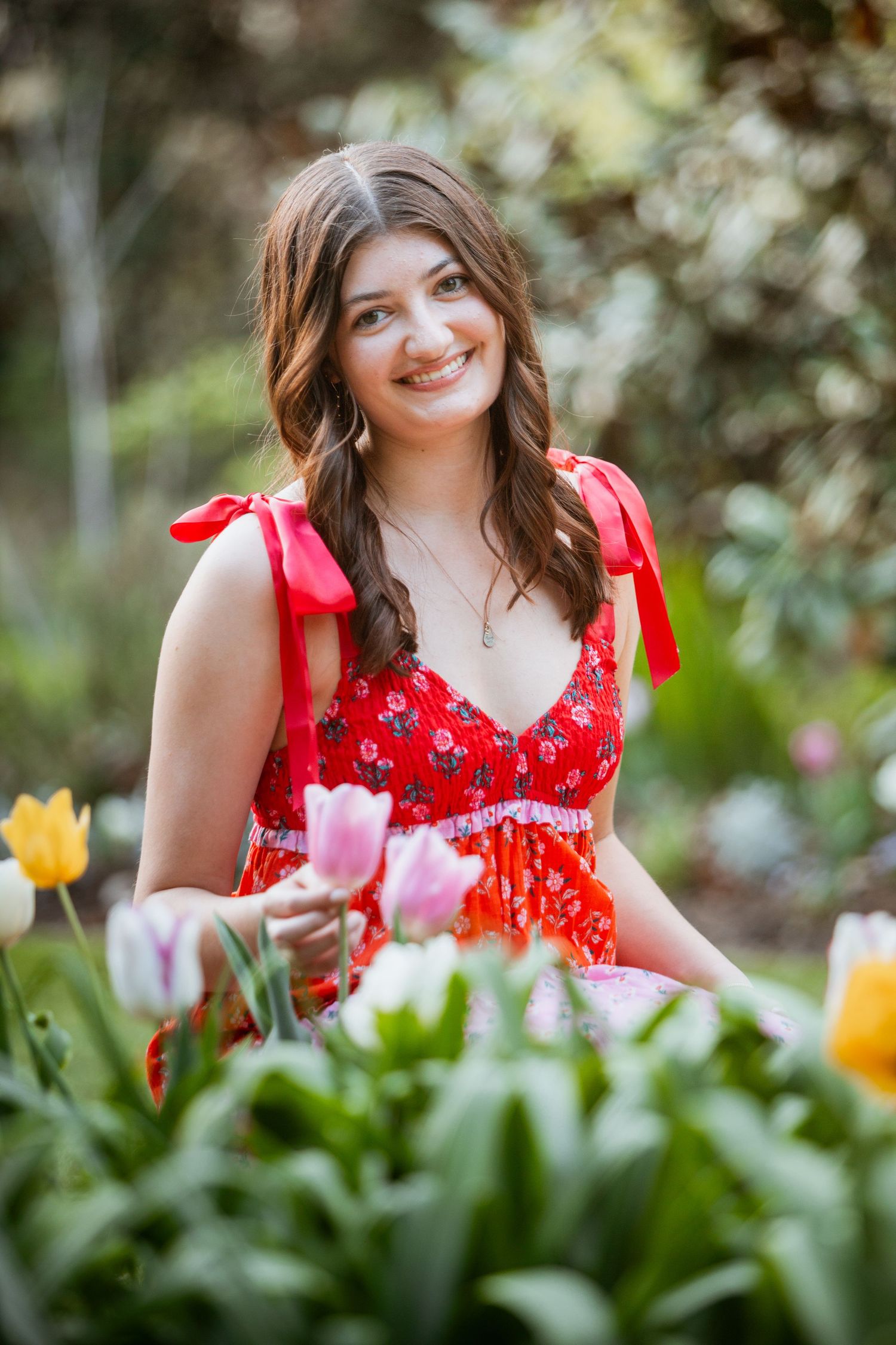 Young woman in red floral dress smiling among colorful tulips in a garden.