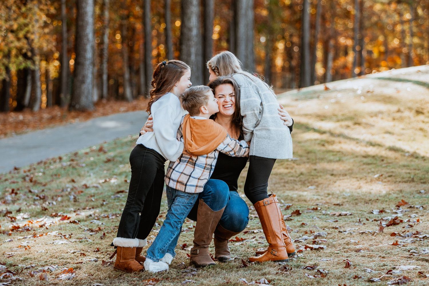 Mother crouching as three children embrace her warmly in a beautiful autumn outdoor setting.