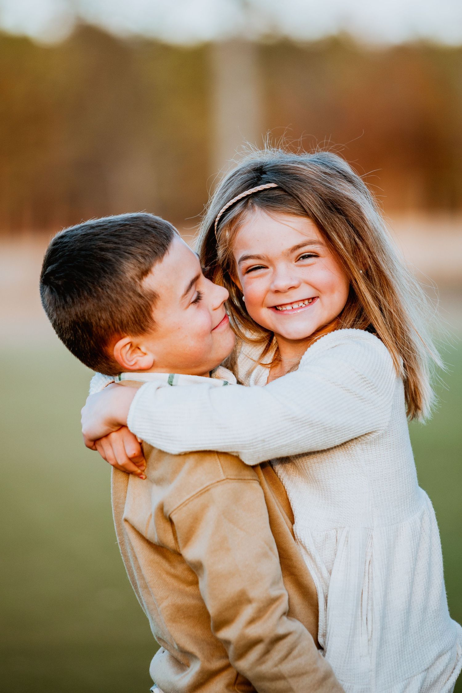 Young boy kissing smiling girl on the cheek while hugging outdoors.