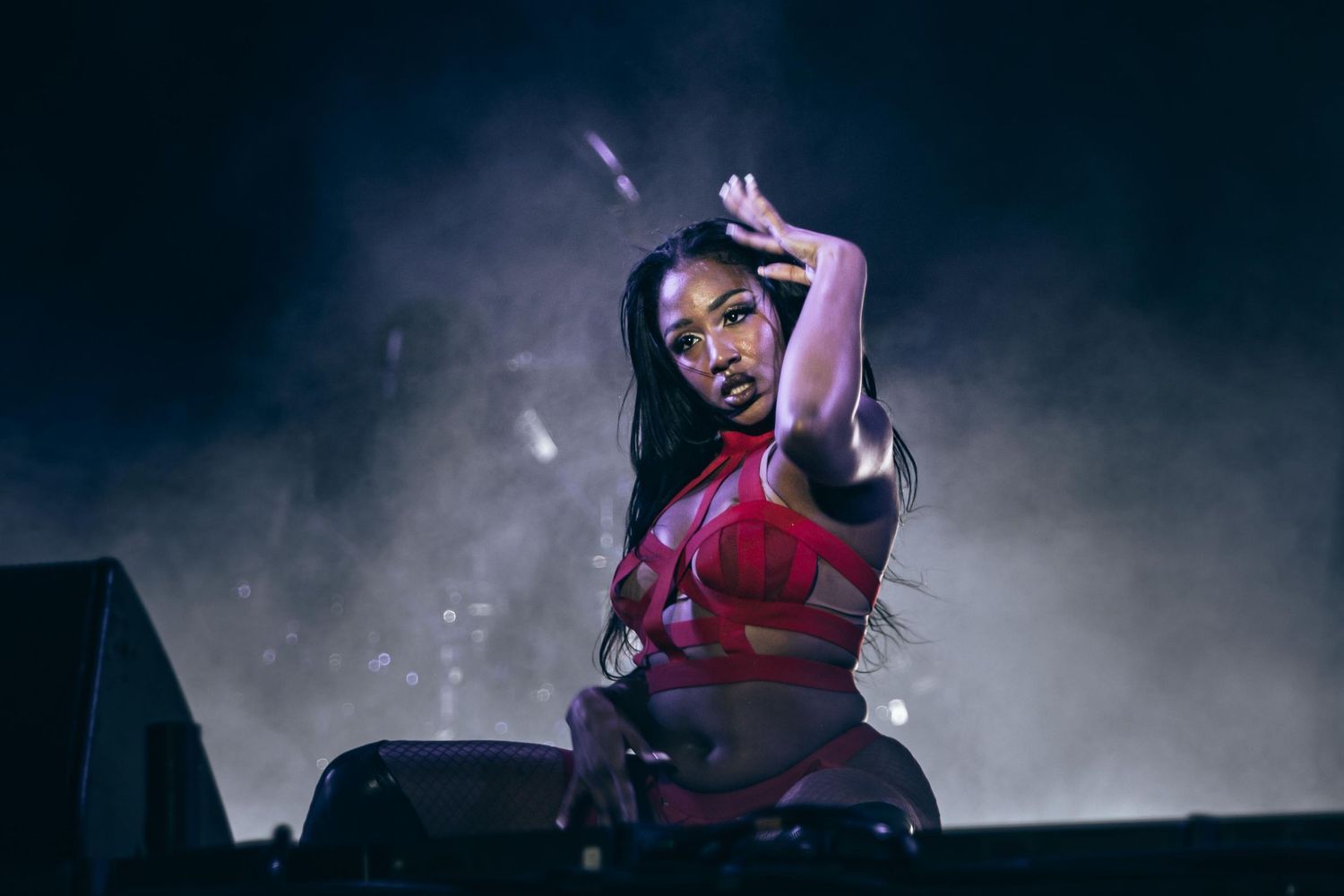 Female performer in red outfit dancing on smoky concert stage.