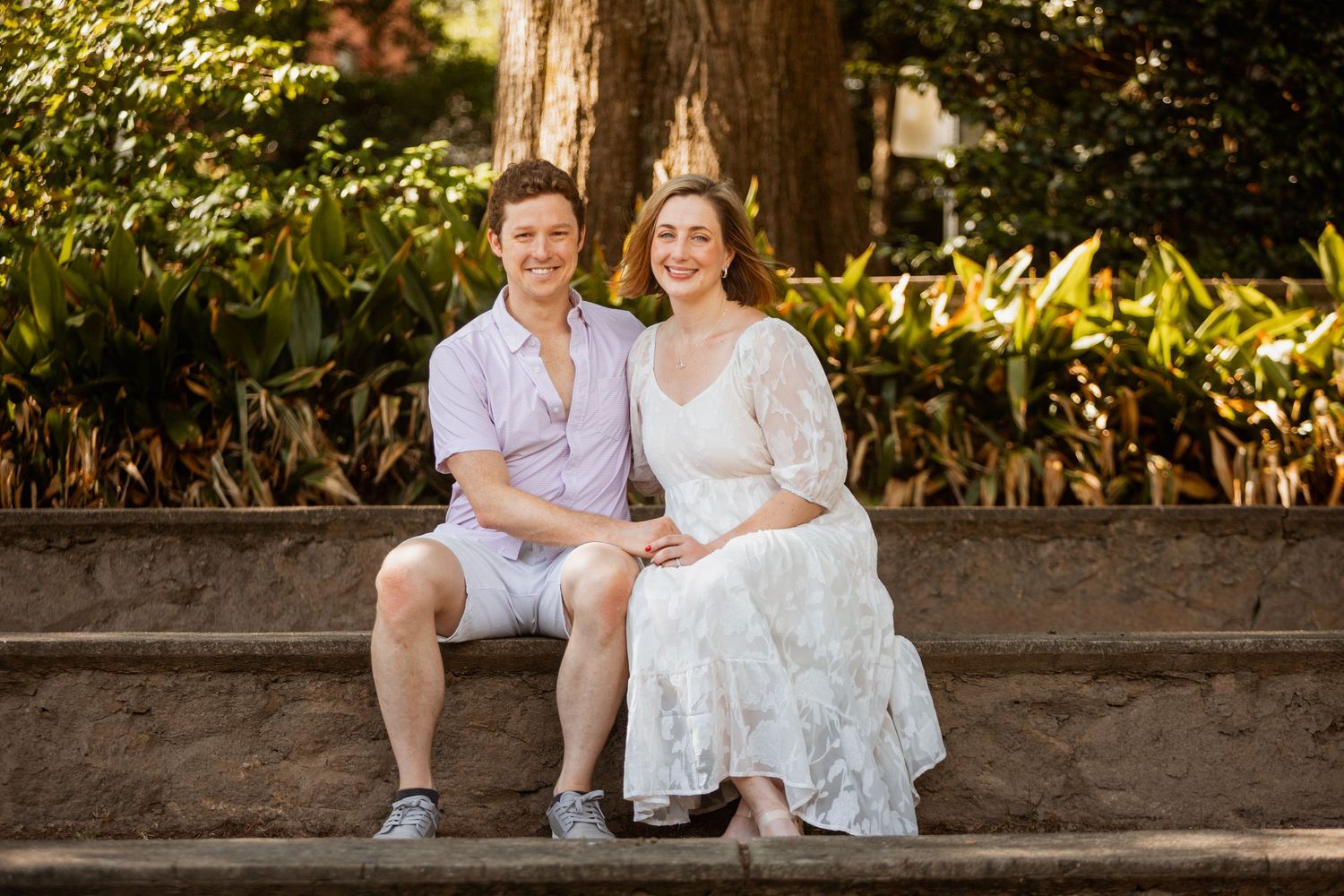 Smiling couple sitting together on stone steps surrounded by beautiful garden greenery.
