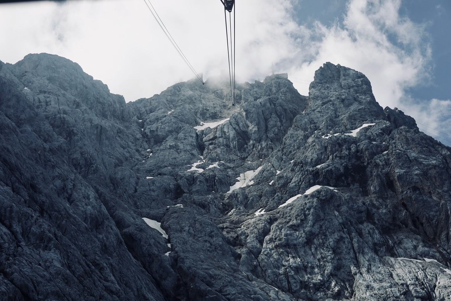 A cable car wire descending toward rugged rocky mountain peaks shrouded in clouds.