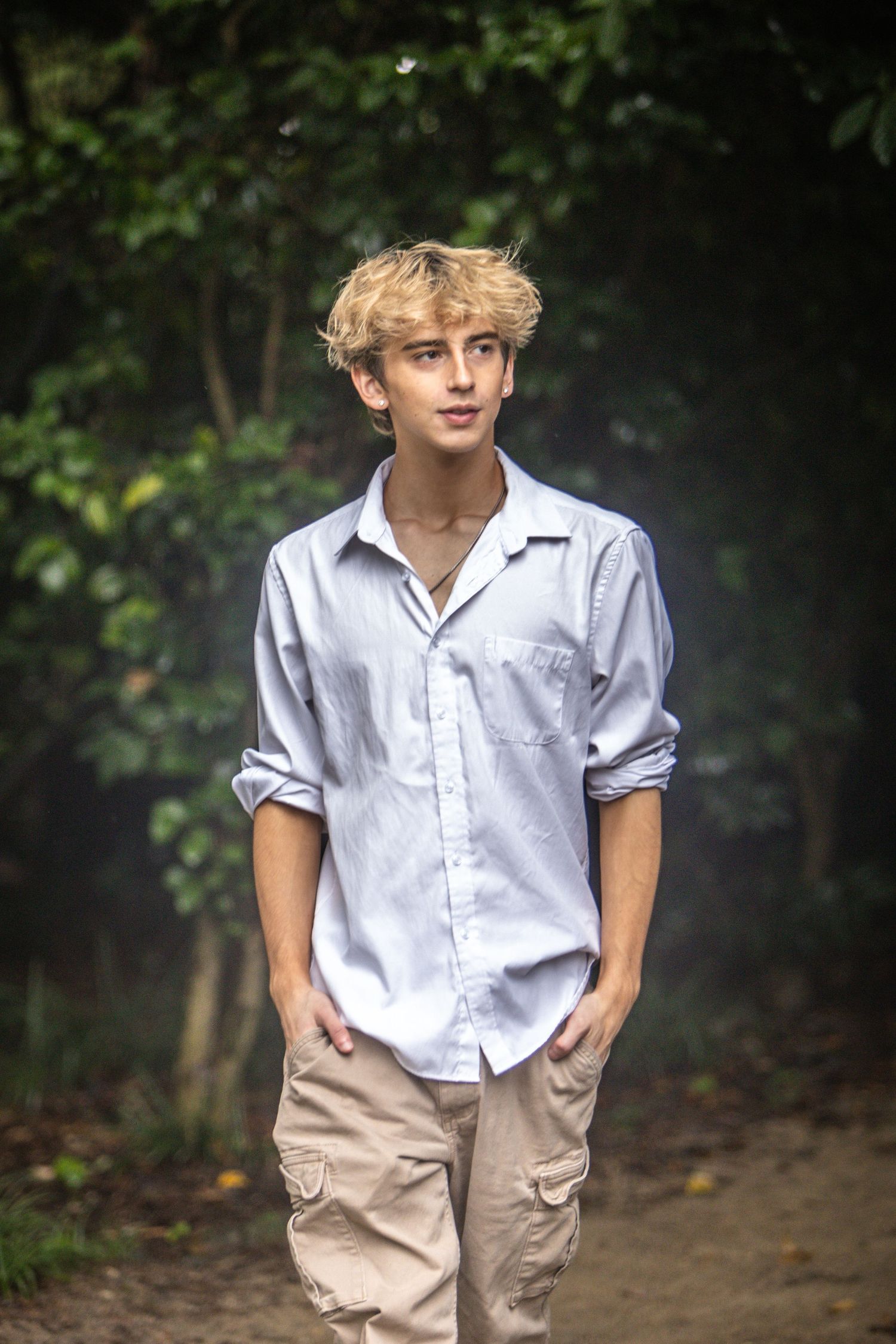Teenage boy with blonde hair in light blue shirt walking on forest path.
