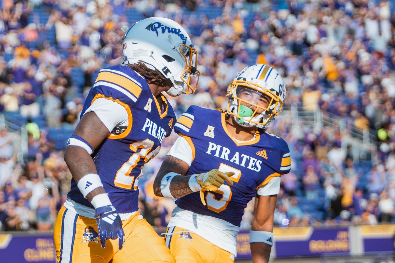 Two ECU Pirates football players celebrate together on the field during a home game.