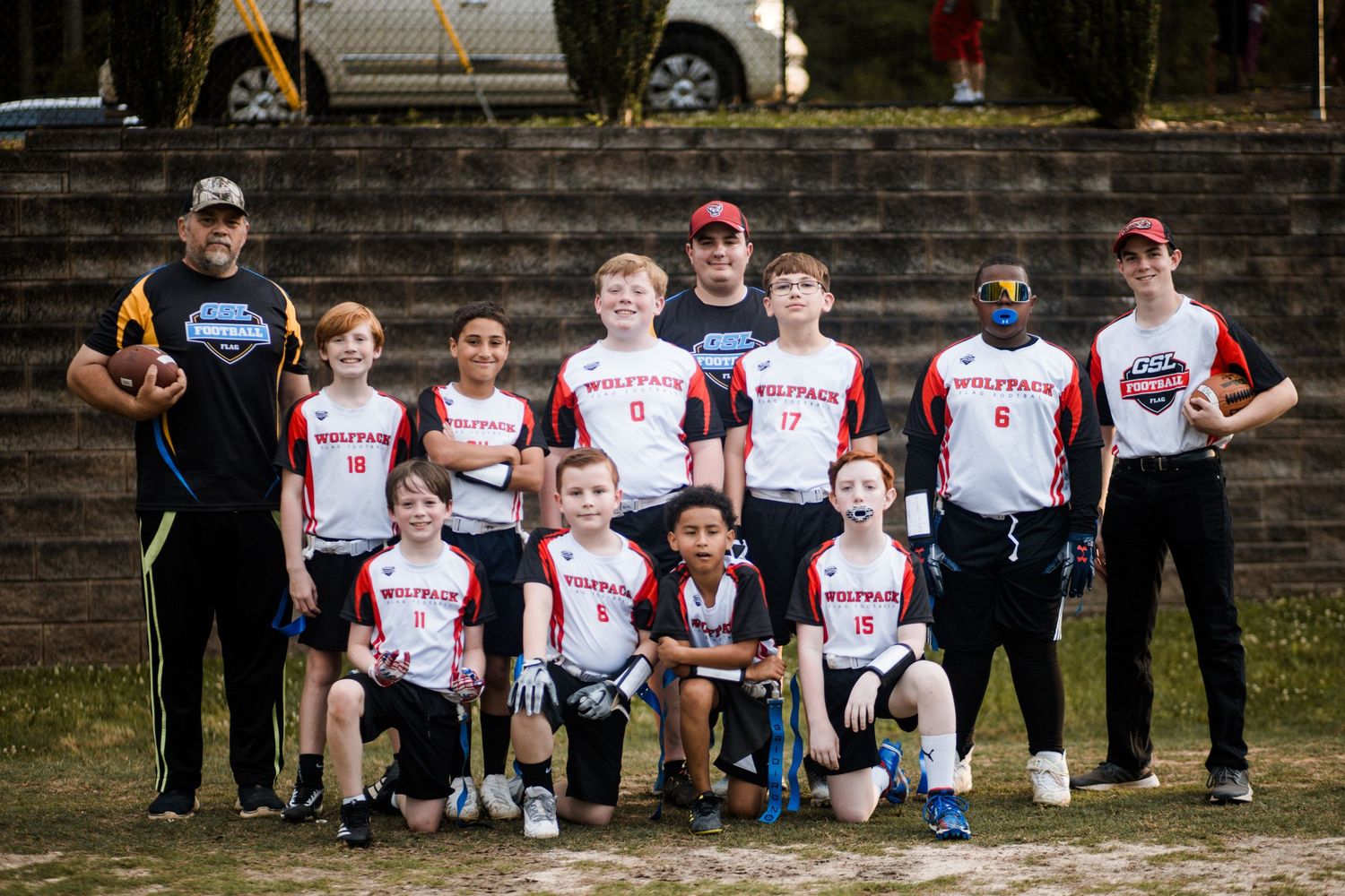 Youth baseball team in red and white Wolfpack uniforms posing with coaches on a dirt field.