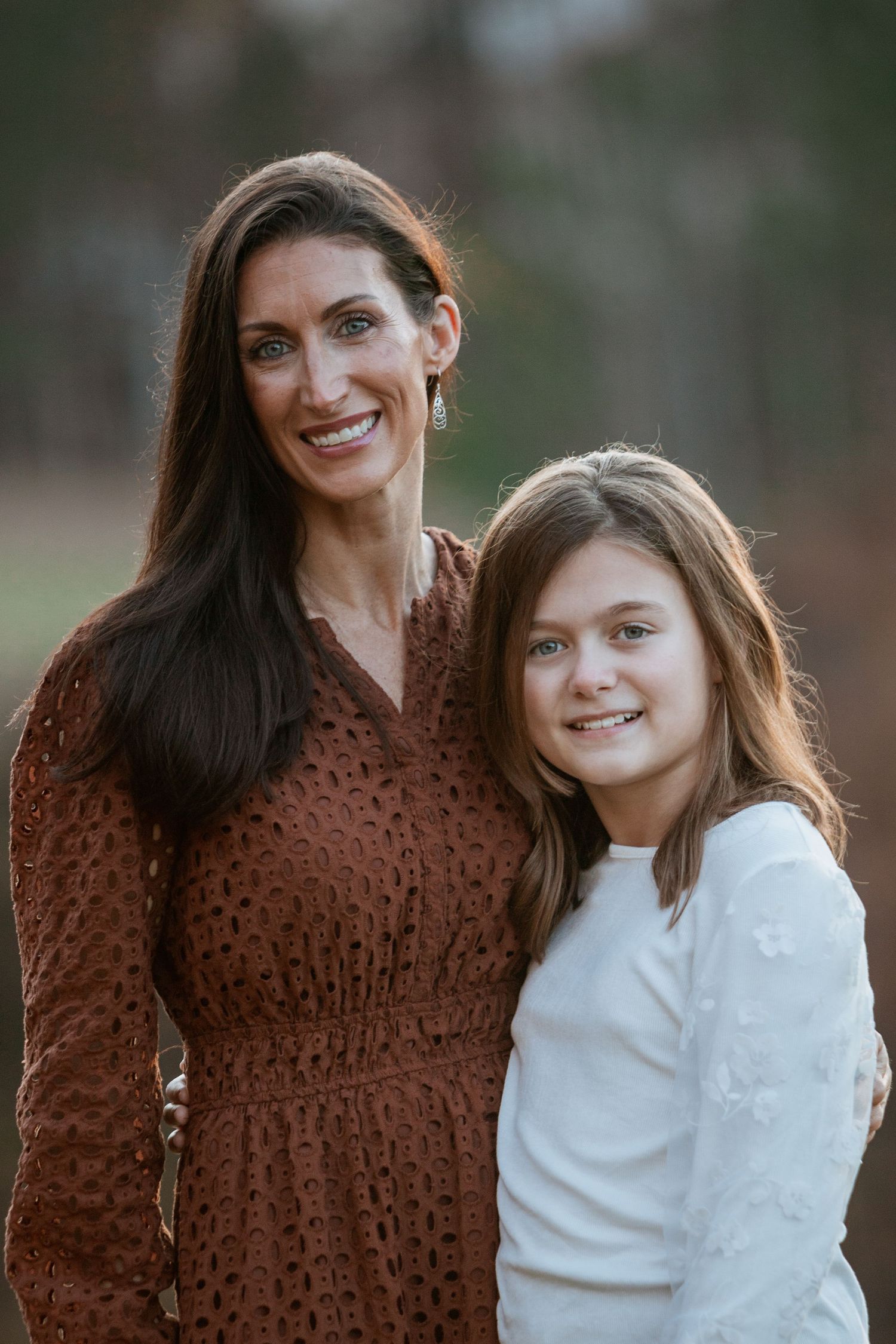 Smiling mother and daughter portrait outdoors in autumn light, wearing brown and white.