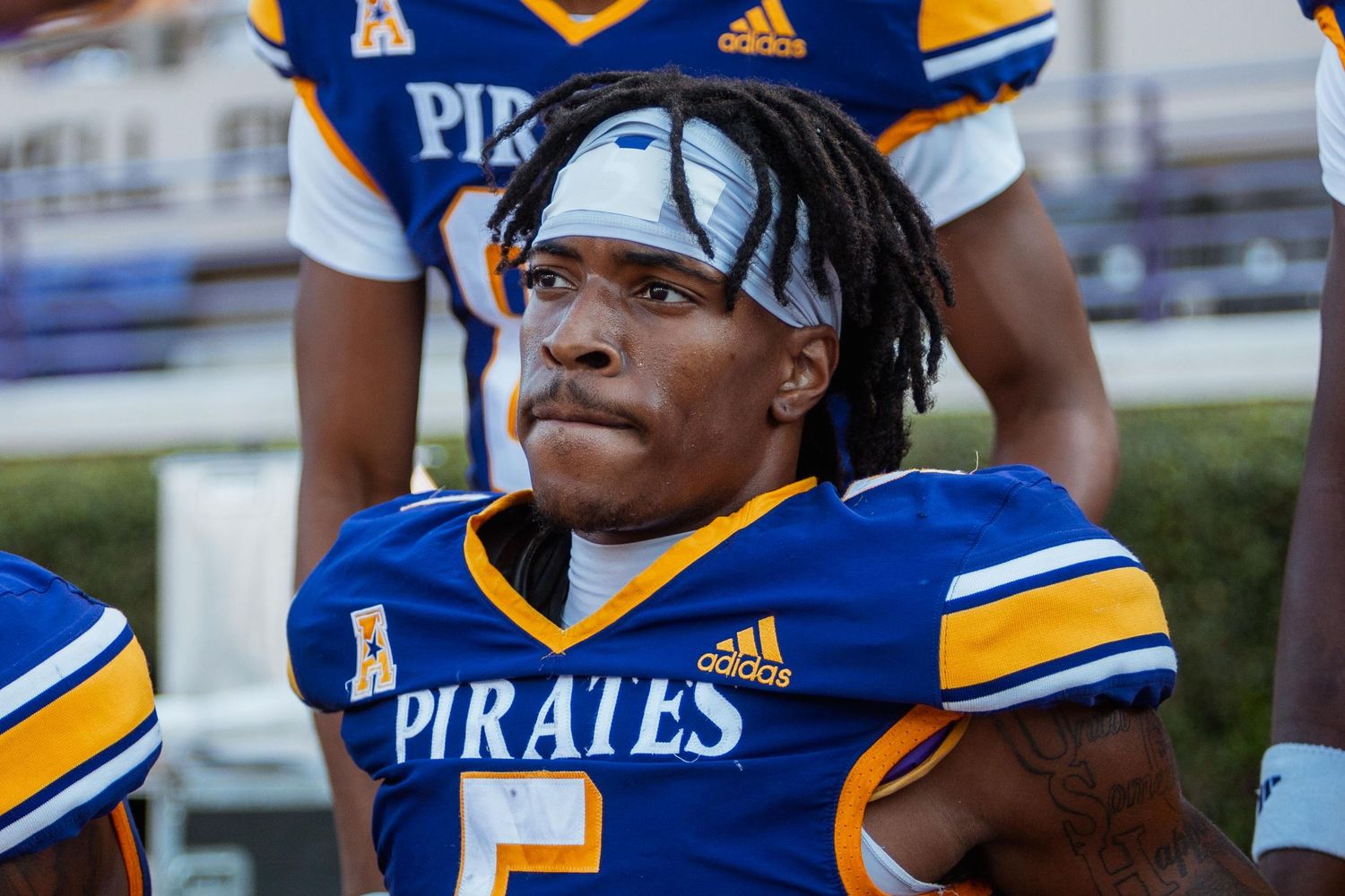 Young football player in blue Pirates jersey number 5 sitting on bench during game day.