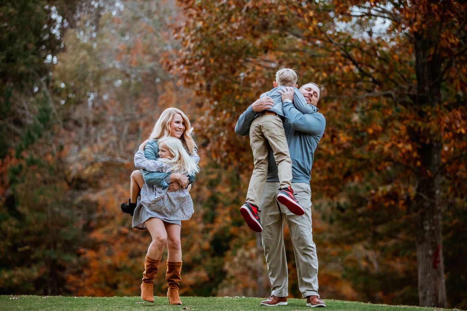 Parents playfully lifting their children in a colorful autumn outdoor family photo session.