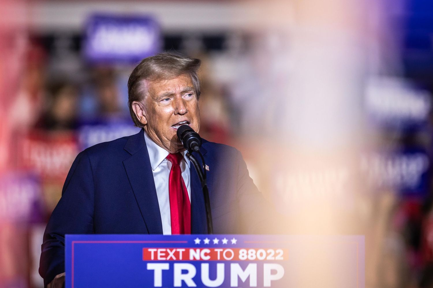 Donald Trump speaks into a microphone at a Trump Vance campaign rally podium in North Carolina.